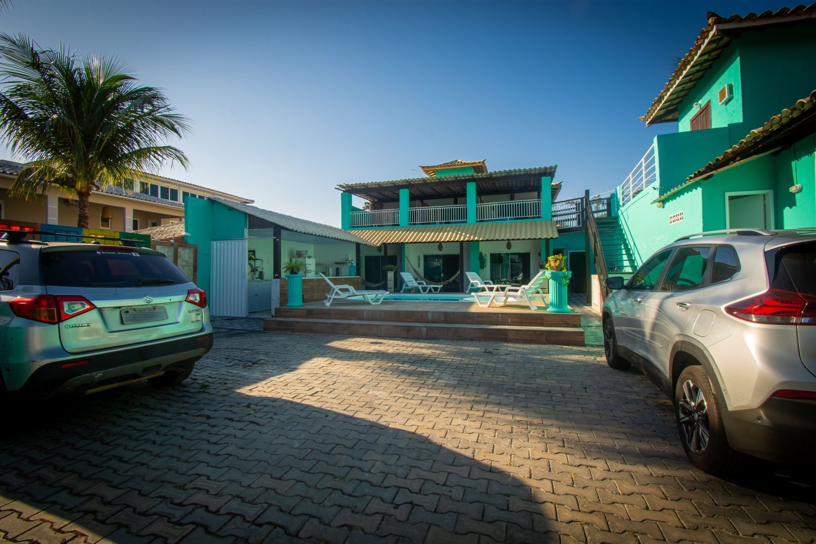 Alguns carros estão estacionados em frente a uma casa verde.