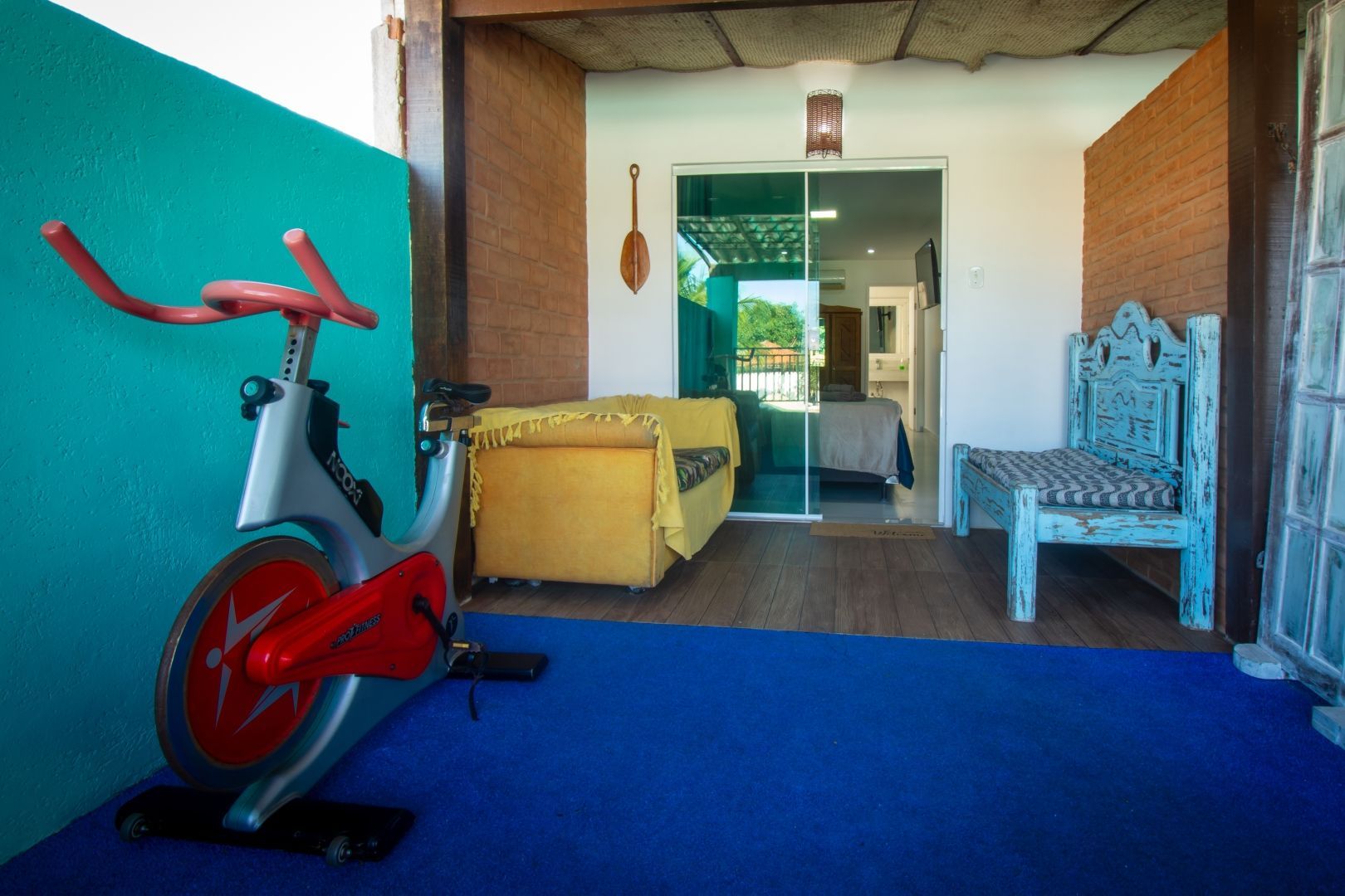 Uma bicicleta ergométrica vermelha está em uma sala ao lado de uma cadeira