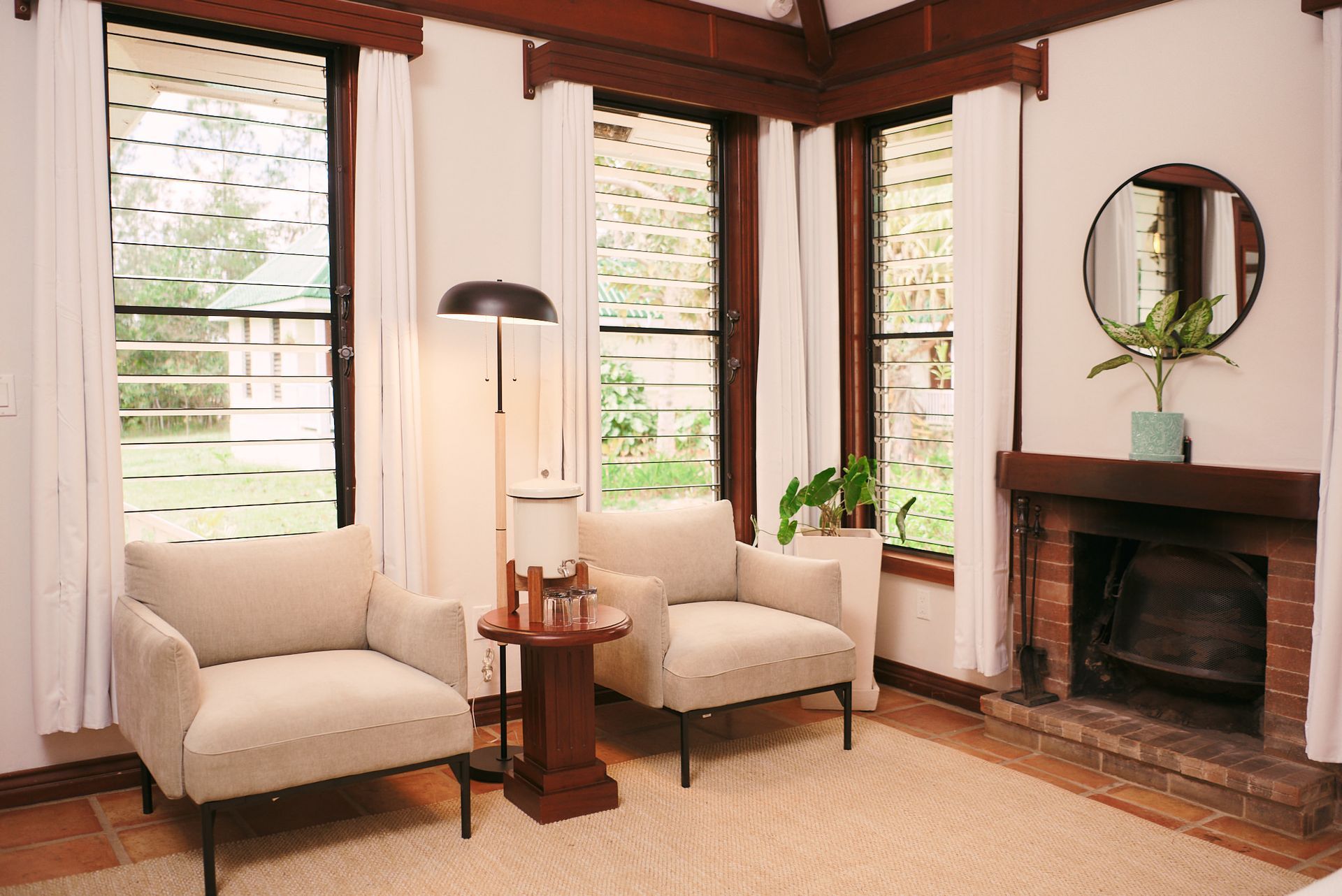 a living room with two chairs , a table , a fireplace and a mirror .