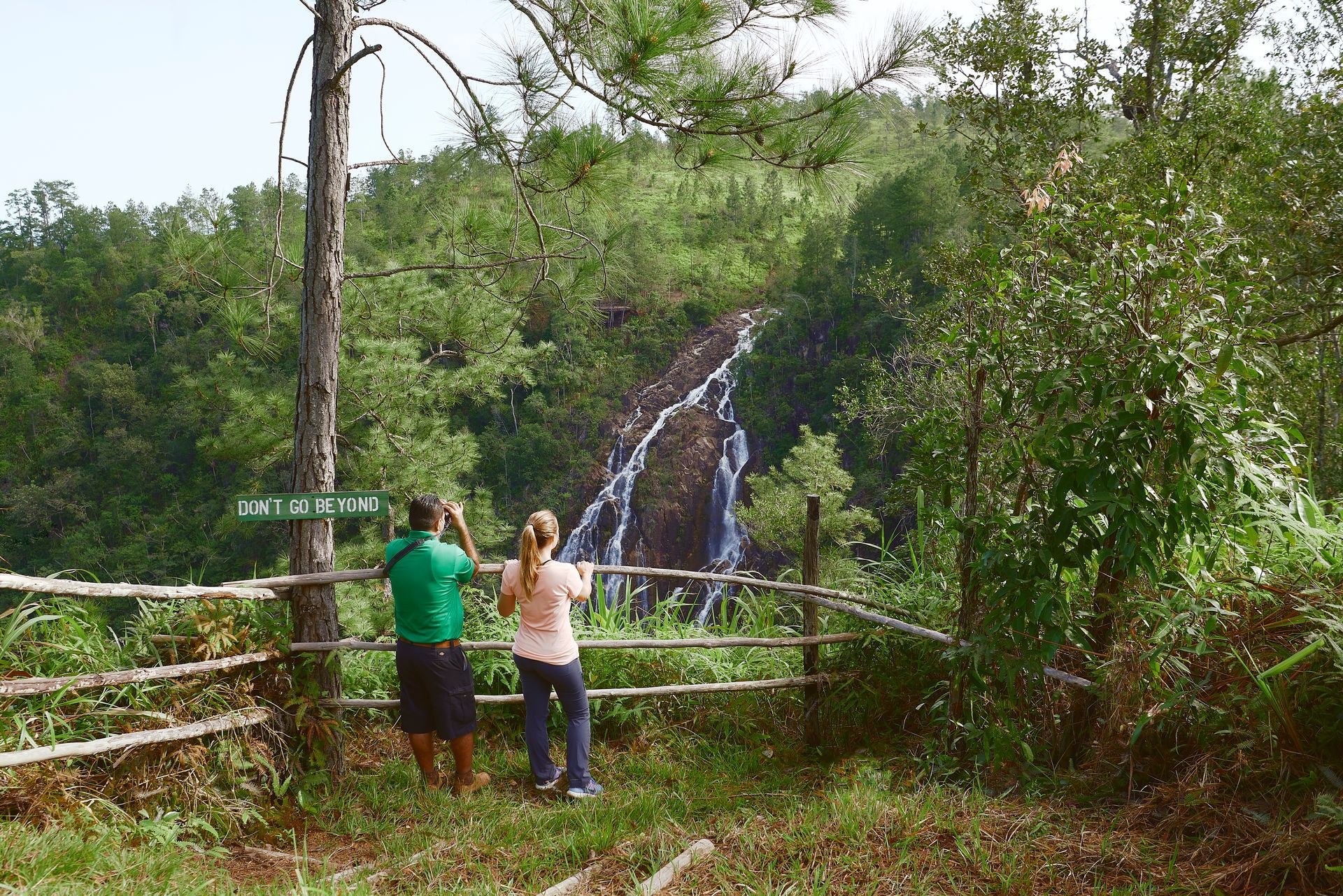 a man and a woman are looking at a waterfall behind a fence .
