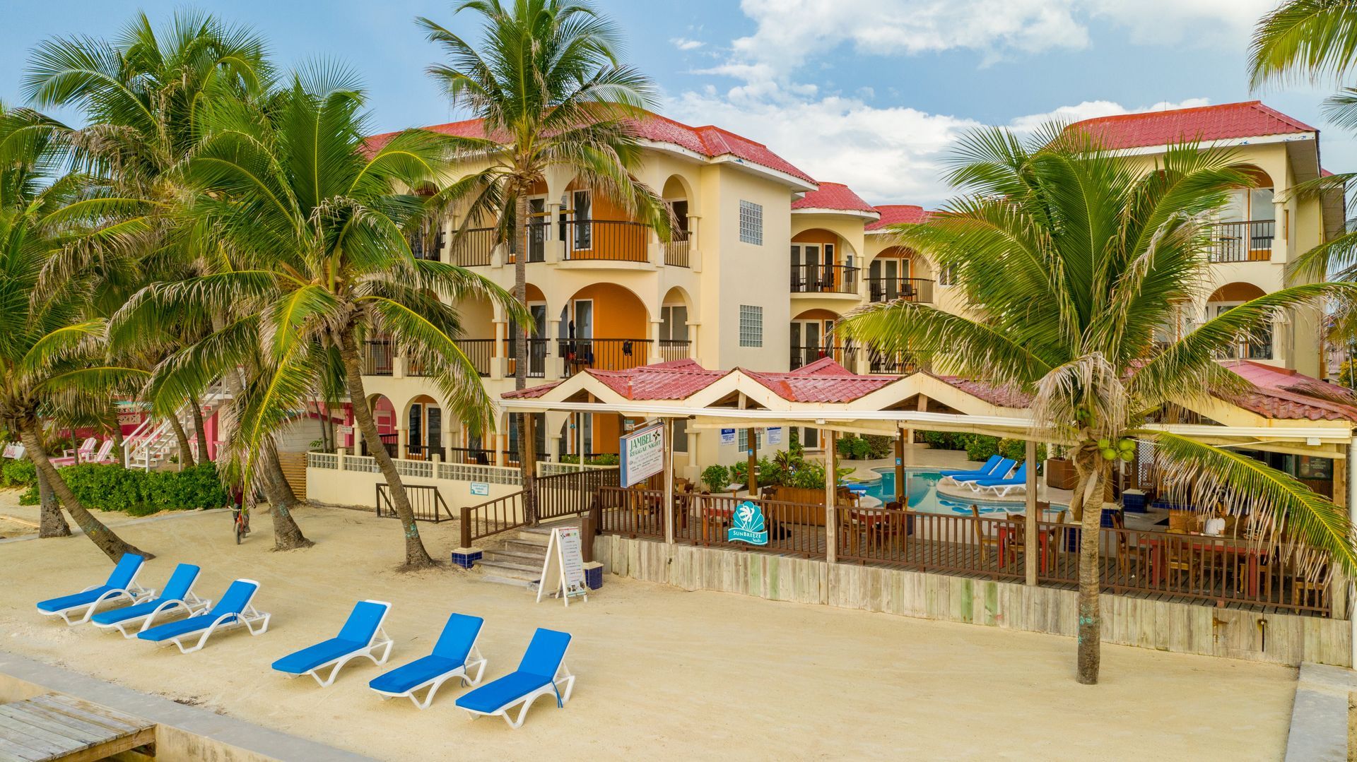 a large building with a red roof is sitting on top of a sandy beach surrounded by palm trees .