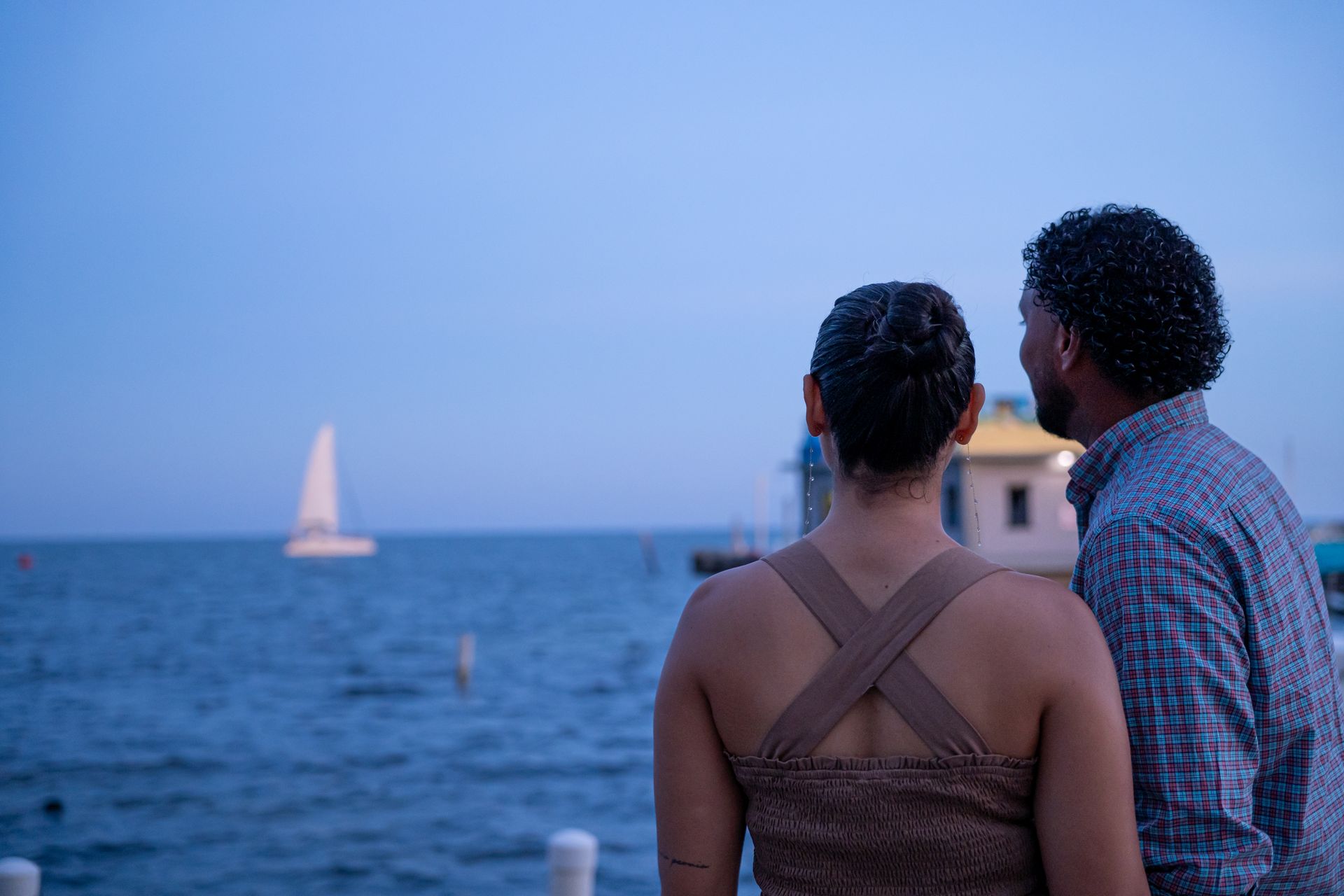A man and a woman are standing on a pier looking at the ocean.