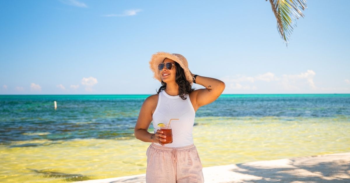 A woman is standing on a beach holding a drink.