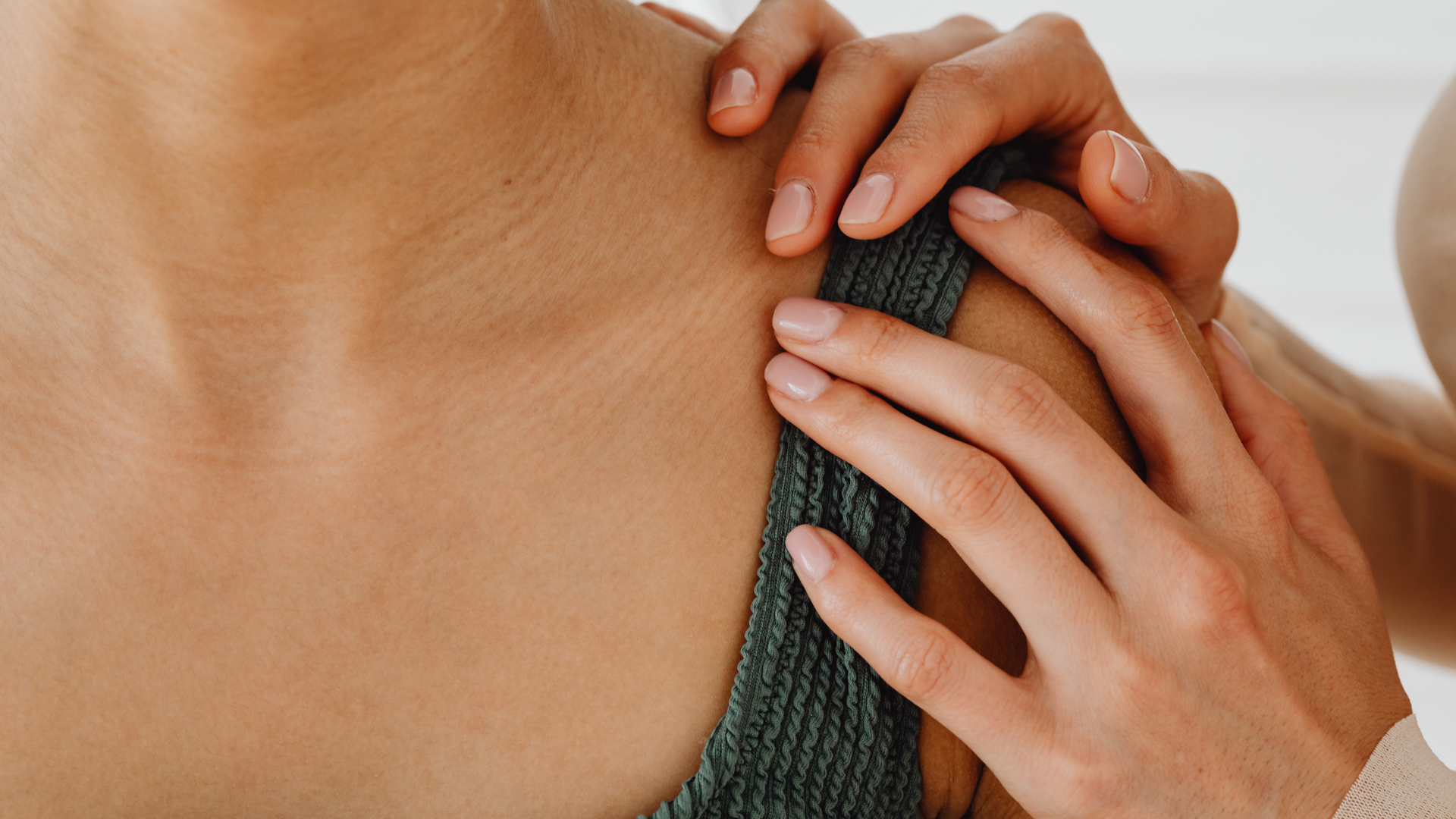 A close-up of a hand gently resting on a person’s shoulder, wearing a dark green textured top.