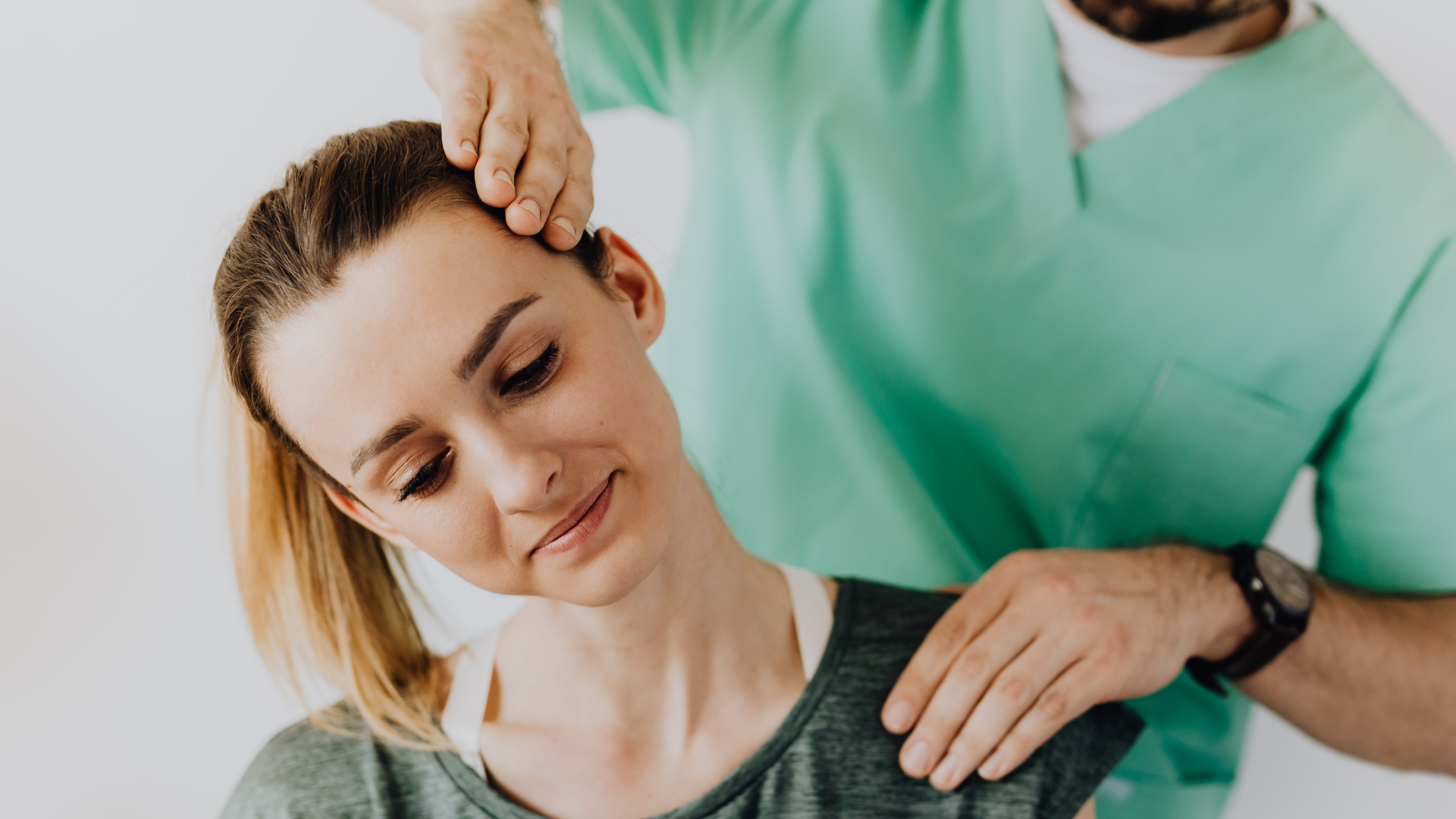 A healthcare provider in green scrubs performs a gentle neck stretch on a patient, who has a calm expression.