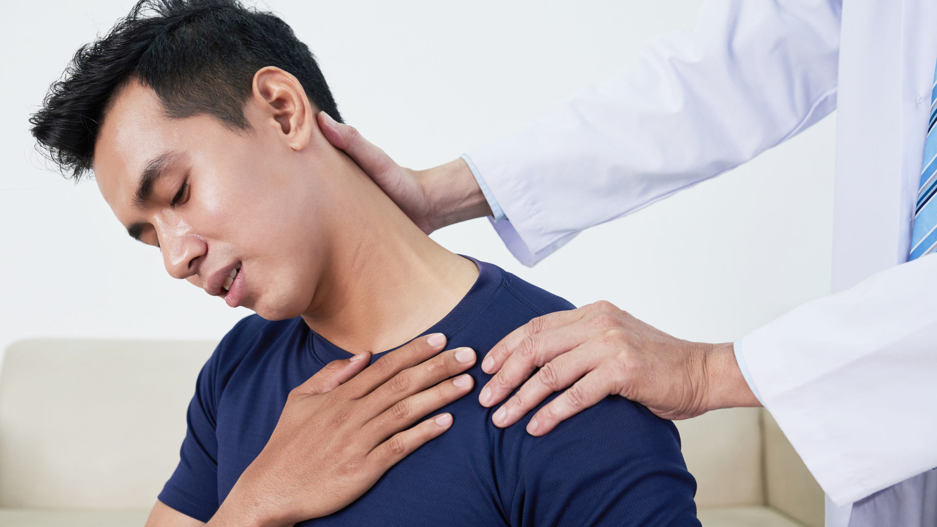 A healthcare provider examines a person's shoulder and neck, who appears to be in discomfort.