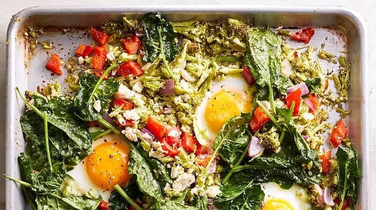 A sheet pan meal with fried eggs, sautéed spinach, diced red peppers, and onions in a light metal baking tray.