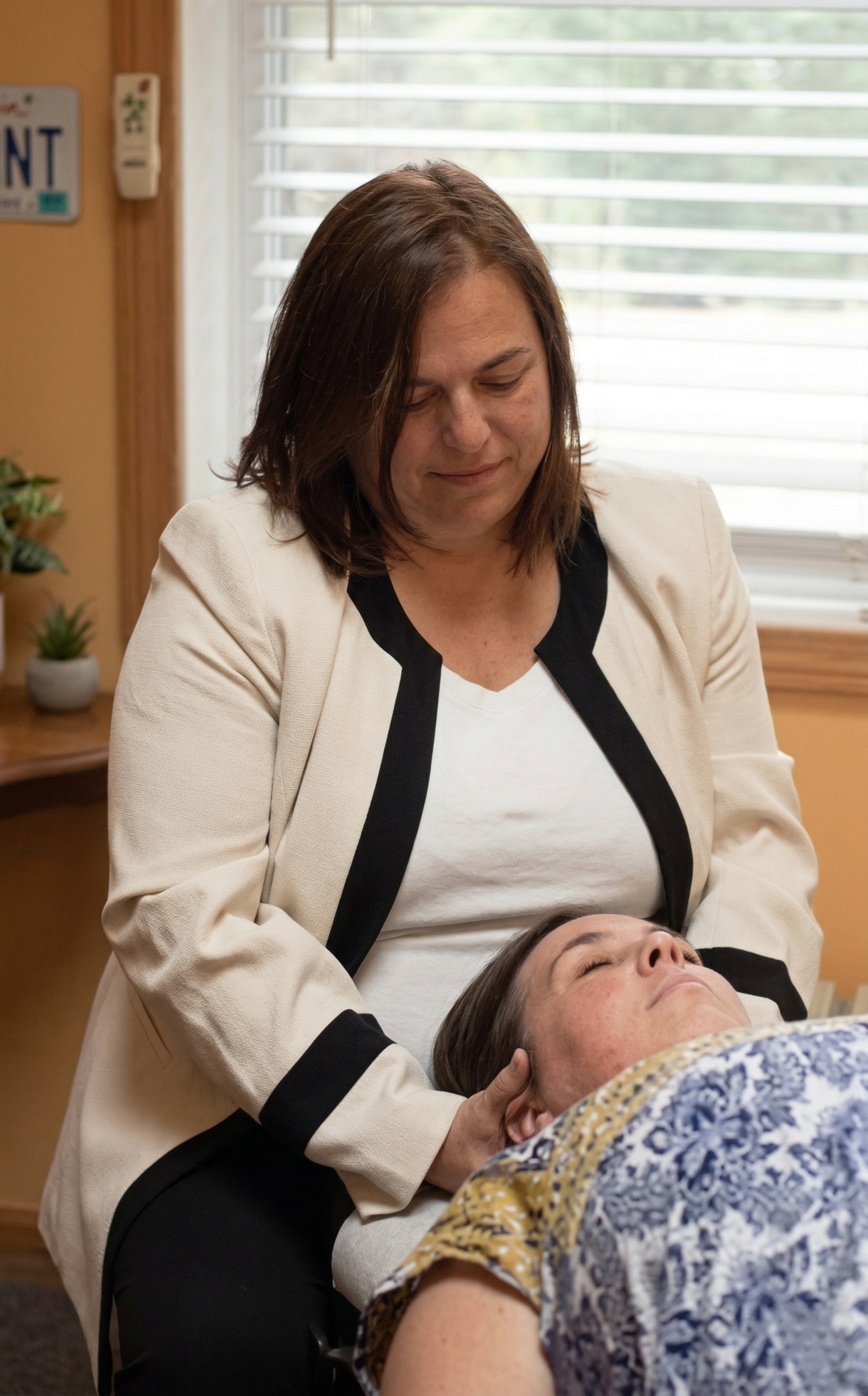 A therapist provides a gentle craniosacral adjustment to a person resting on a table in a calm, indoor setting.