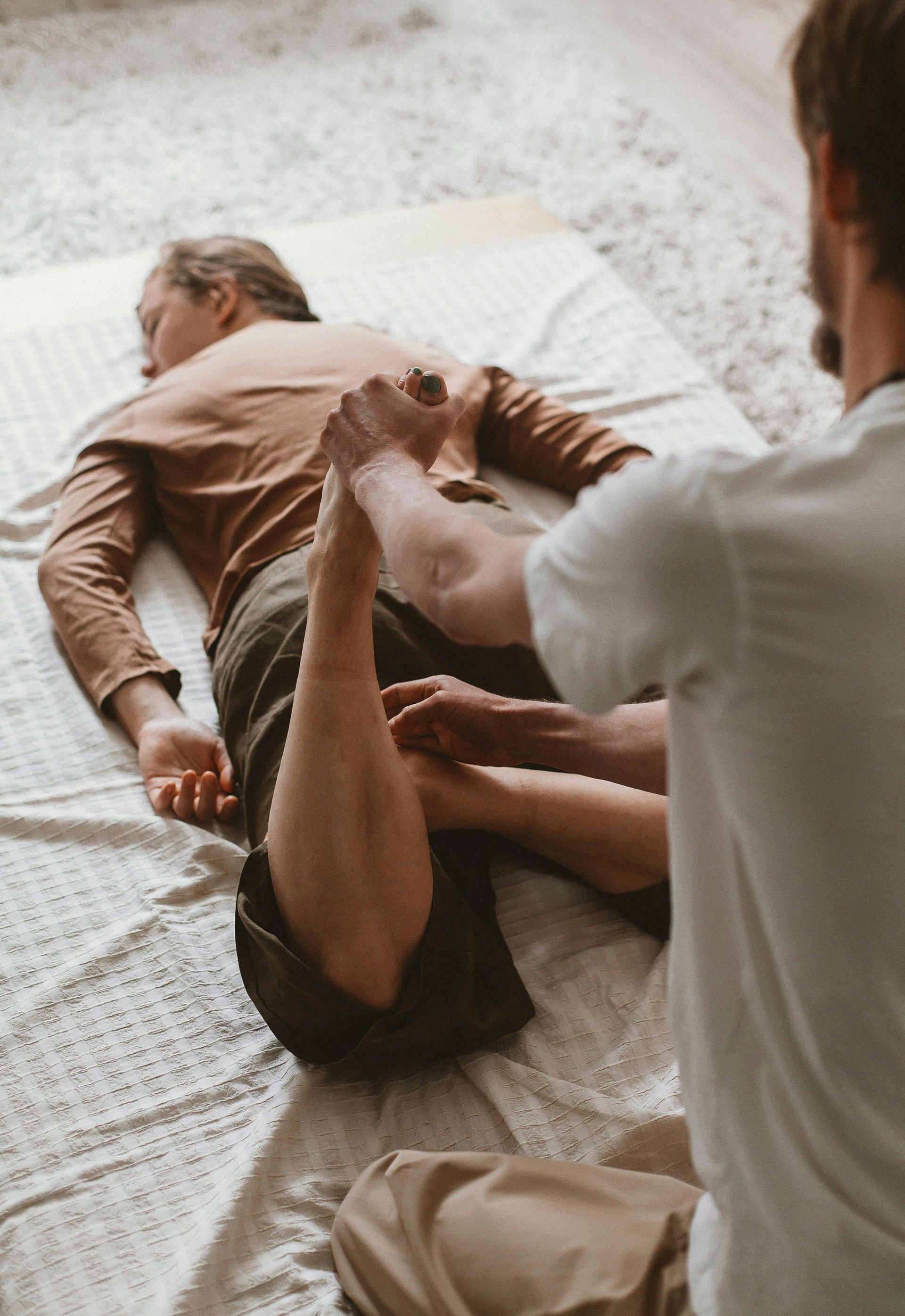 Two people practicing a floor exercise on a carpeted room, one assisting the other by the legs.