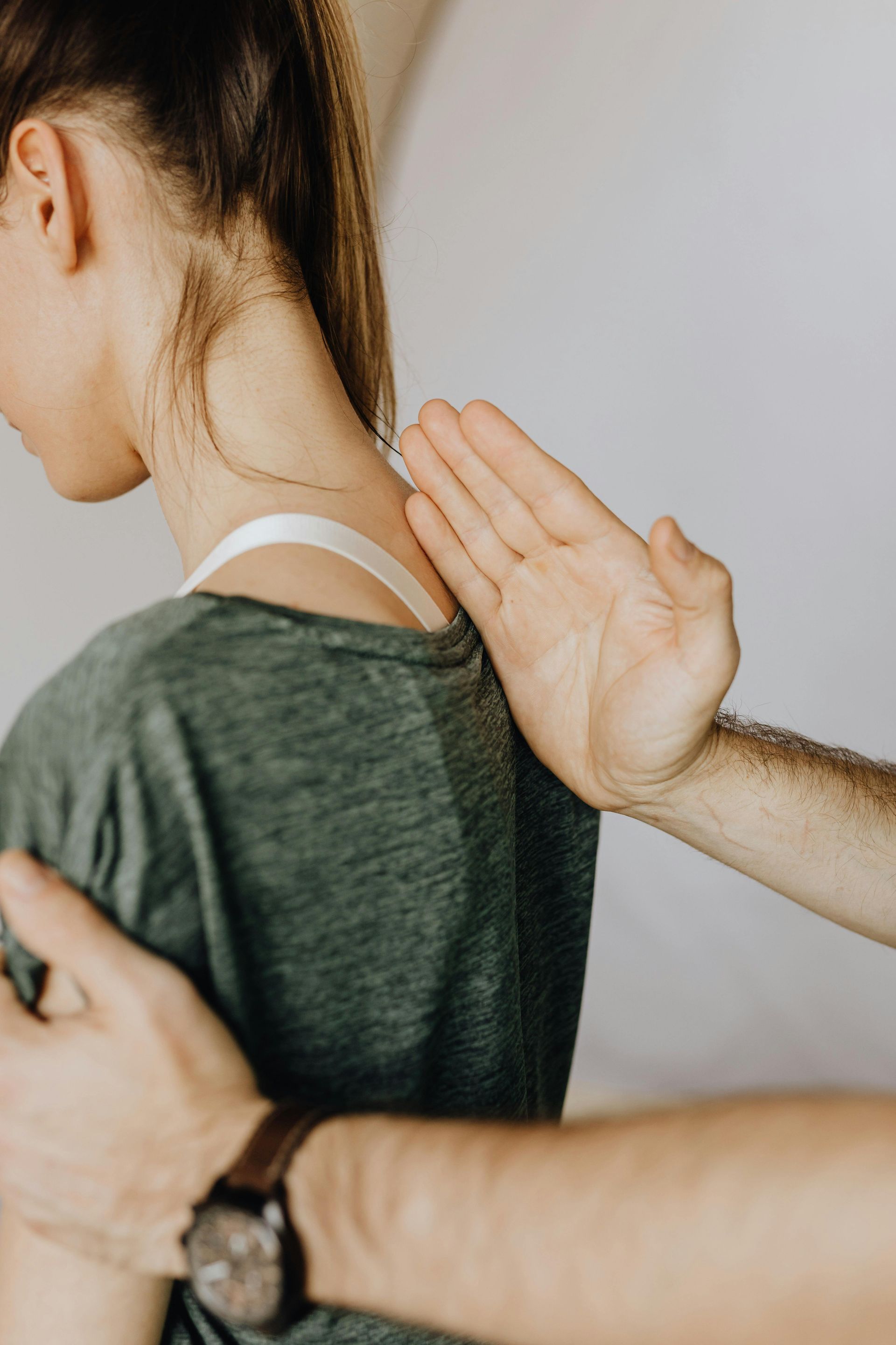 Hands demonstrating shoulder posture on a person in a green shirt, with one hand on the upper back.