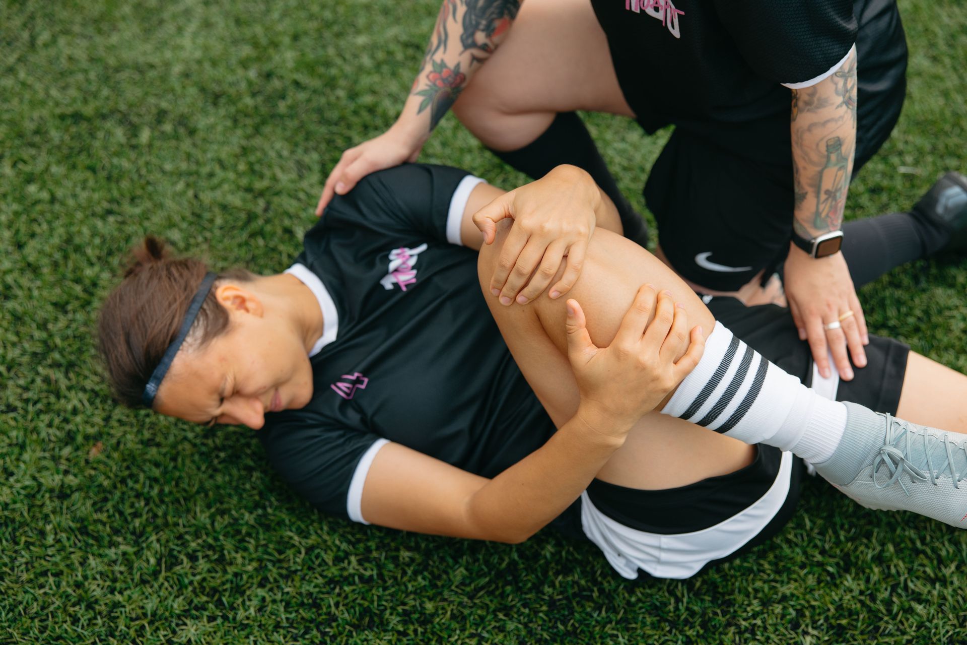 Trainer helping athlete stretch leg on grass field