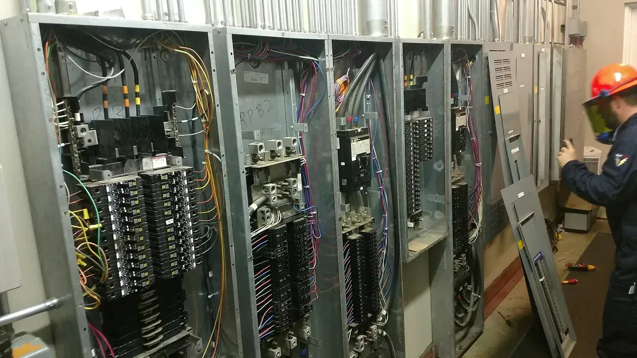 A man wearing a hard hat is working on a electrical panel.