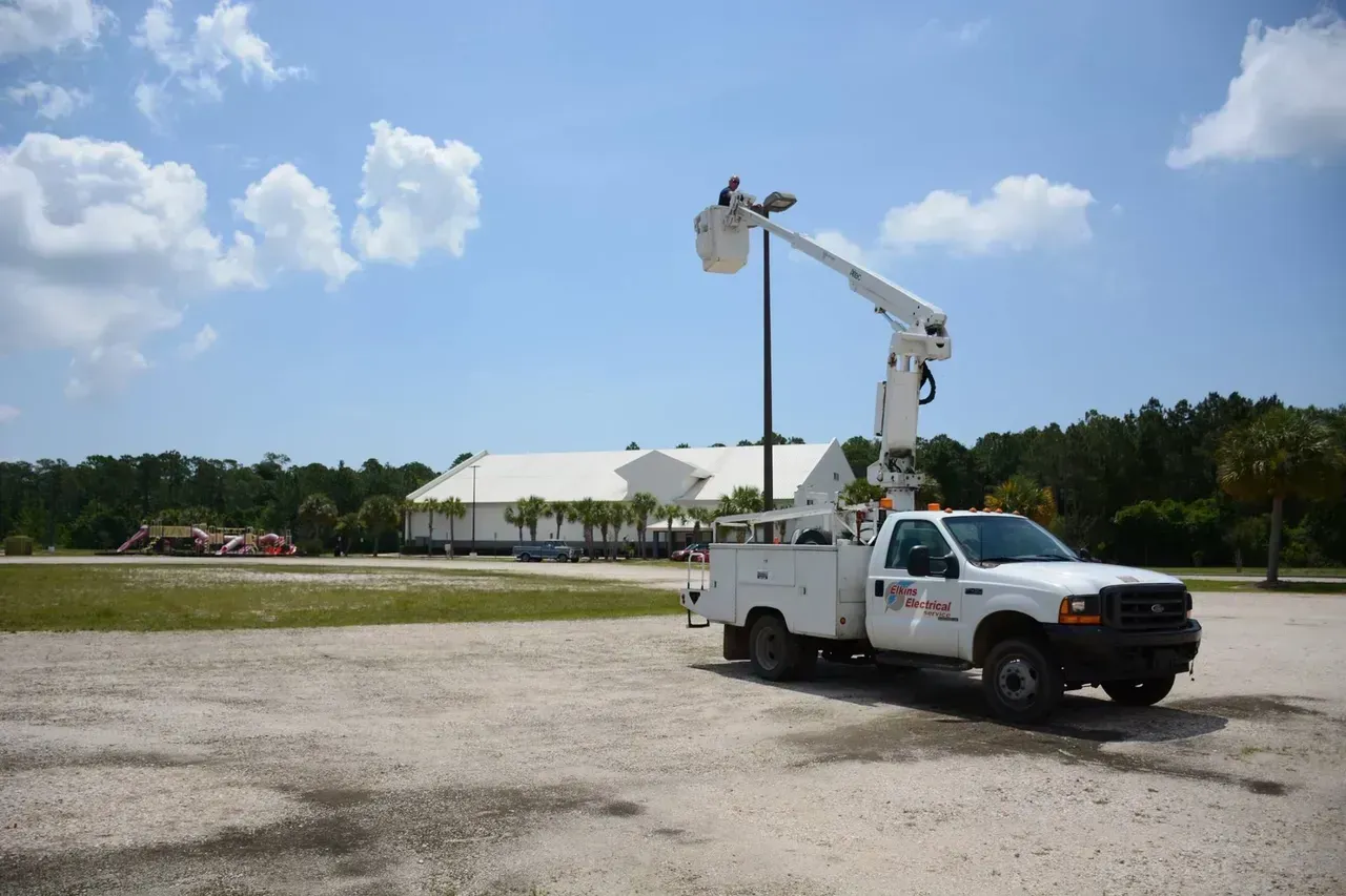 A white truck with a bucket on top of it is parked in a parking lot.