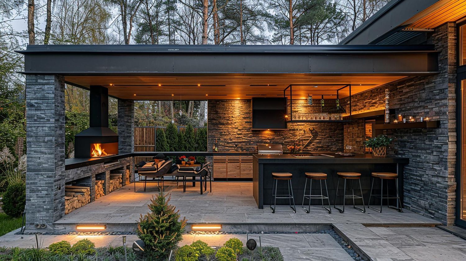 Outdoor kitchen with stone walls, fireplace, bar, and seating, lit by warm lights.