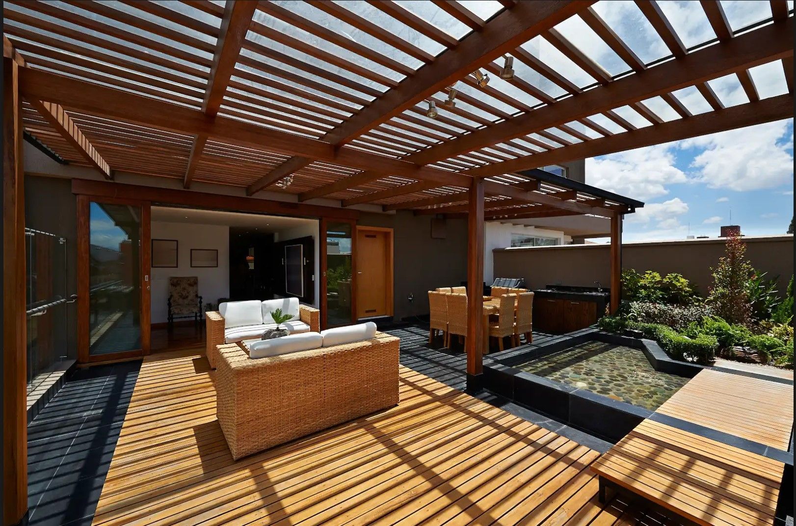 A patio with a pergola and a couch and chairs underneath it.