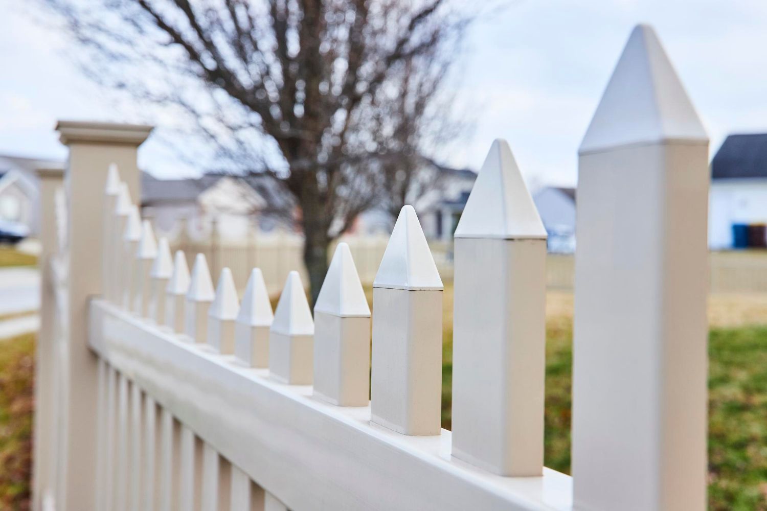 White picket fence with pointed tops, in a residential neighborhood.