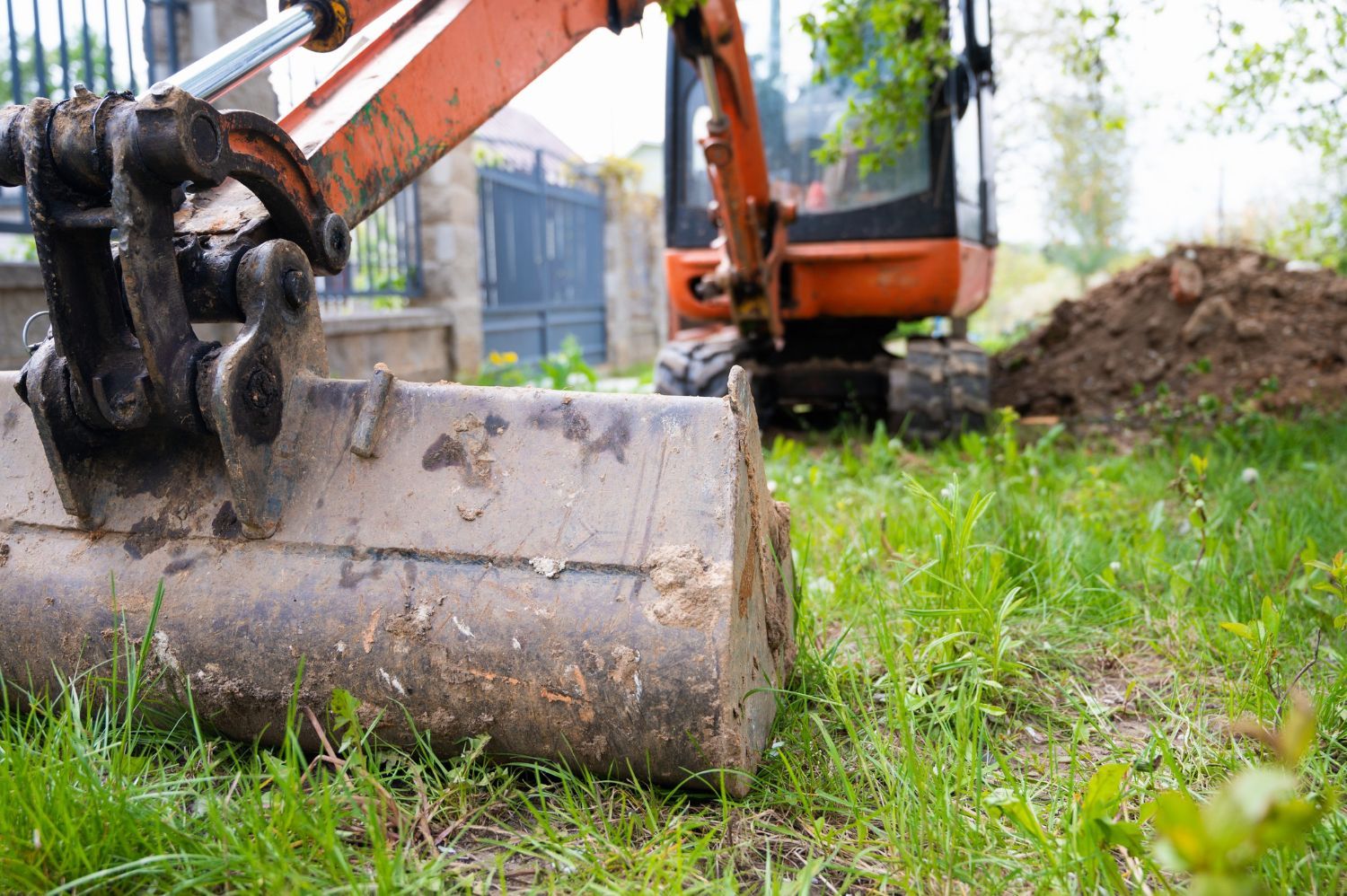 A small excavator is sitting in the grass next to a pile of dirt.