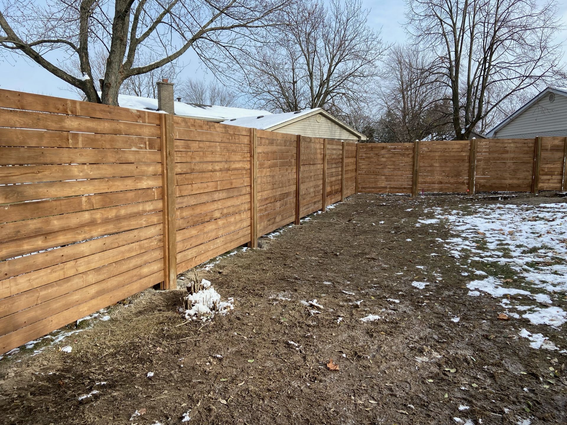 A wooden fence surrounds a snowy yard in front of a house.