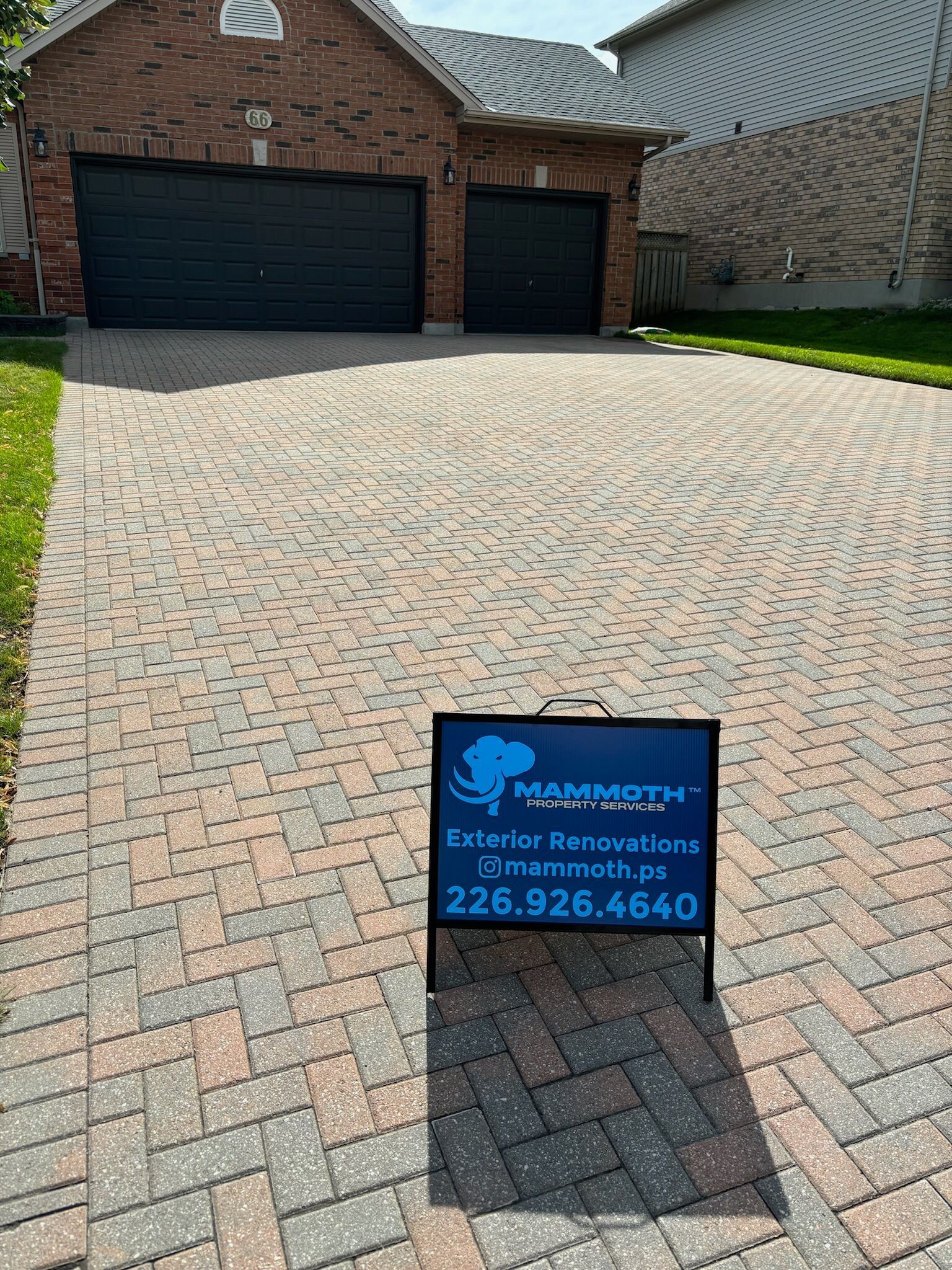 A brick driveway with a sign in front of a house.