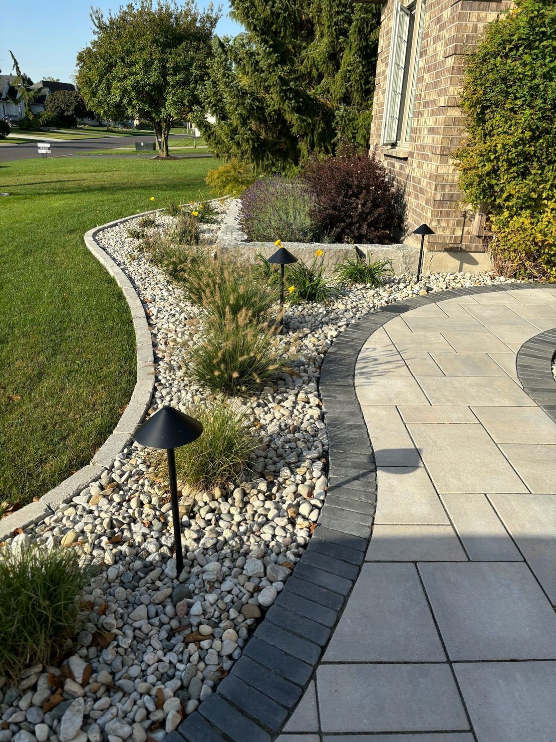 A brick walkway leading to a lush green lawn in a garden.