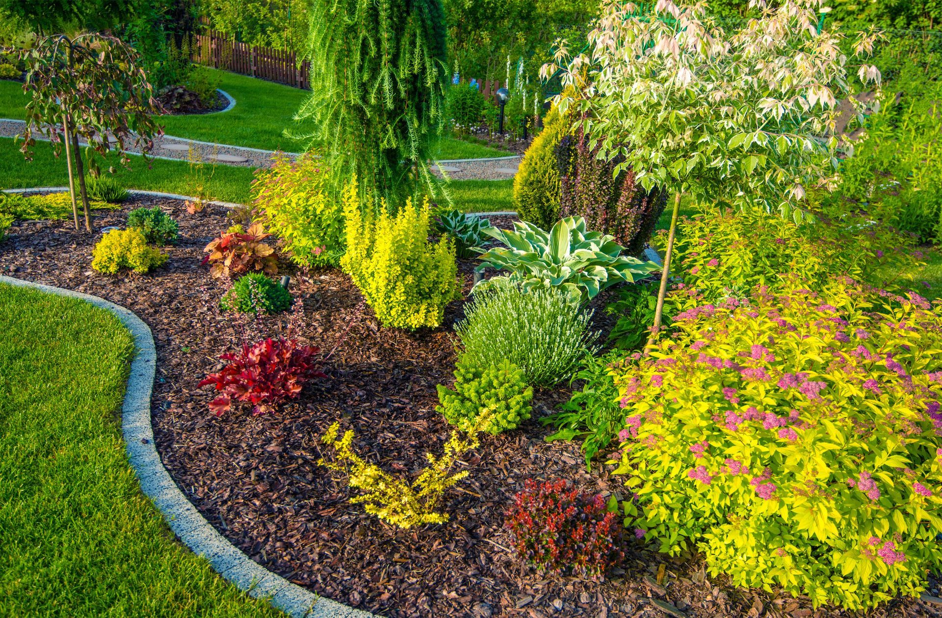 Landscaped garden bed with various colorful shrubs, bordered by a concrete edge and vibrant green lawn.