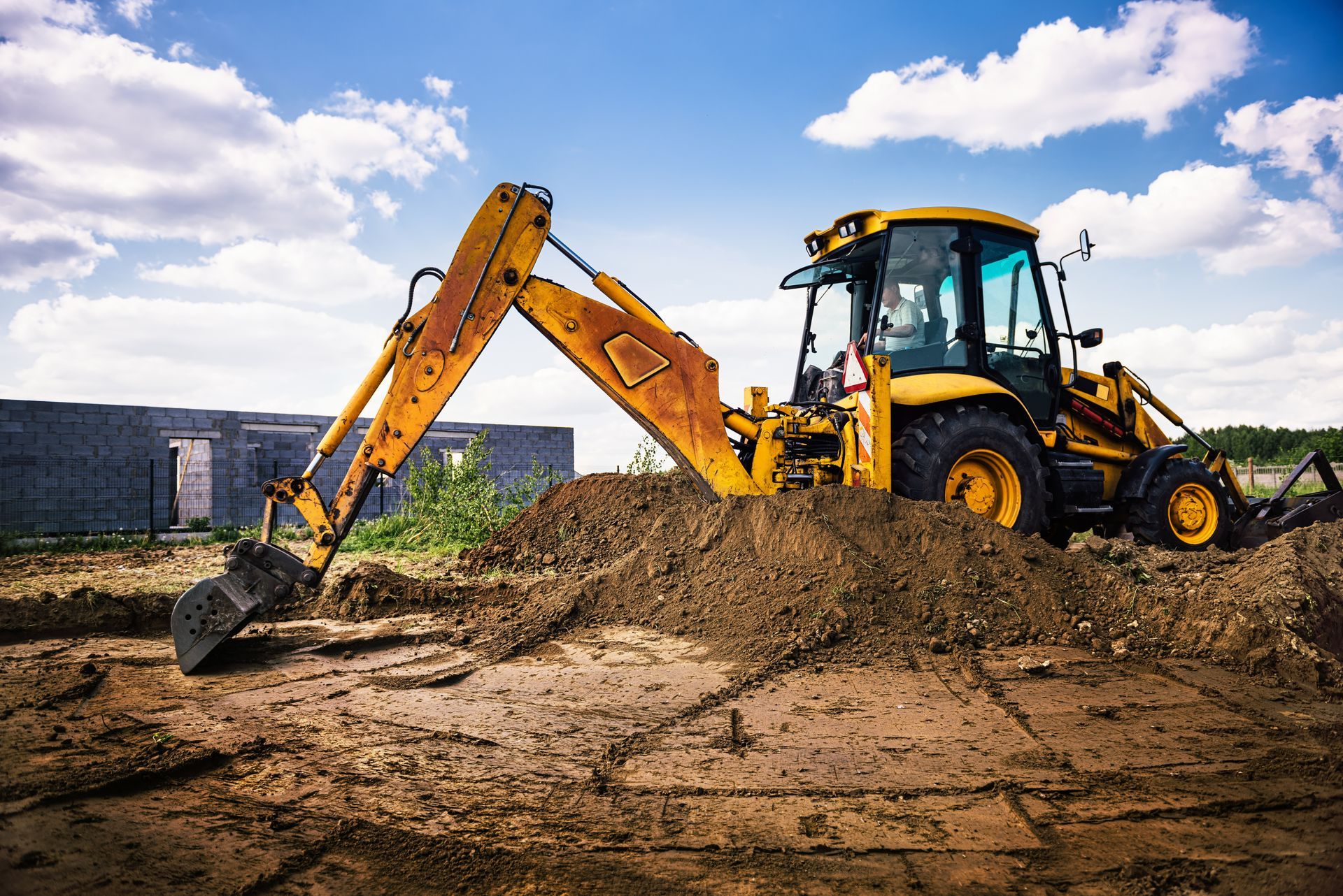 A yellow excavator is digging a hole in a dirt field.