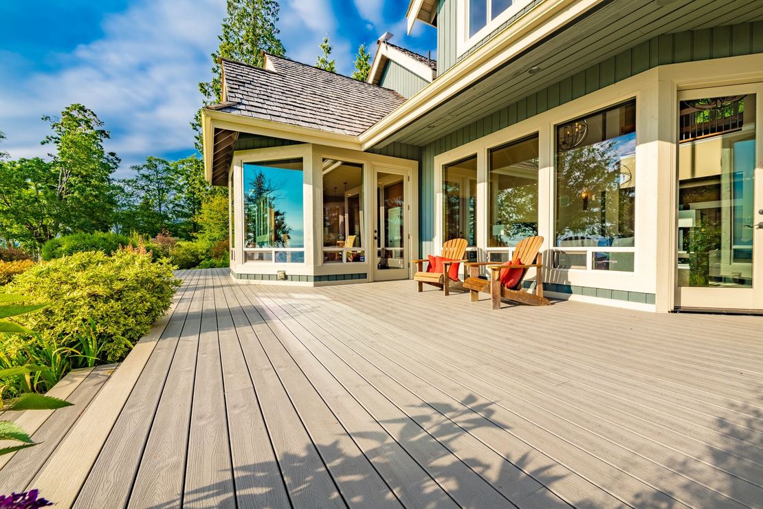 A large house with a wooden deck and chairs in front of it.