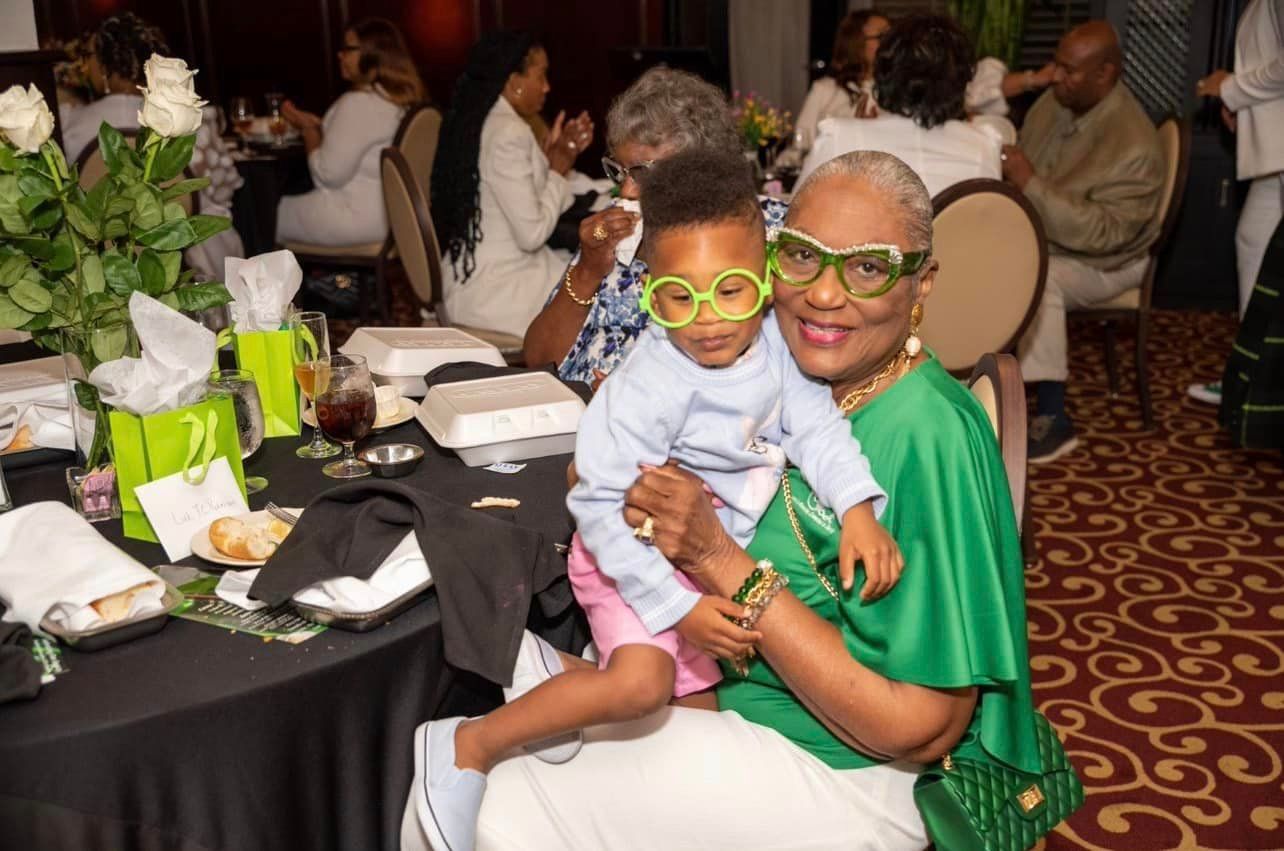 Woman in green holding a child with glasses at a celebratory event.