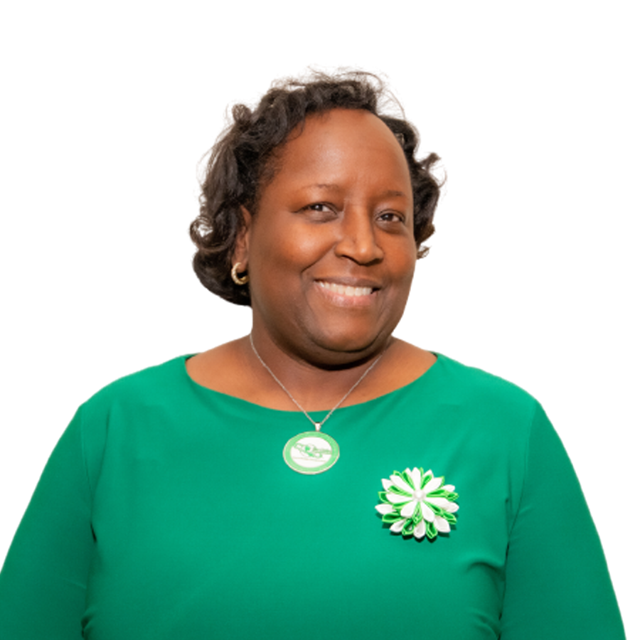 Woman in green top smiling, wearing a necklace and flower pin against a white background.