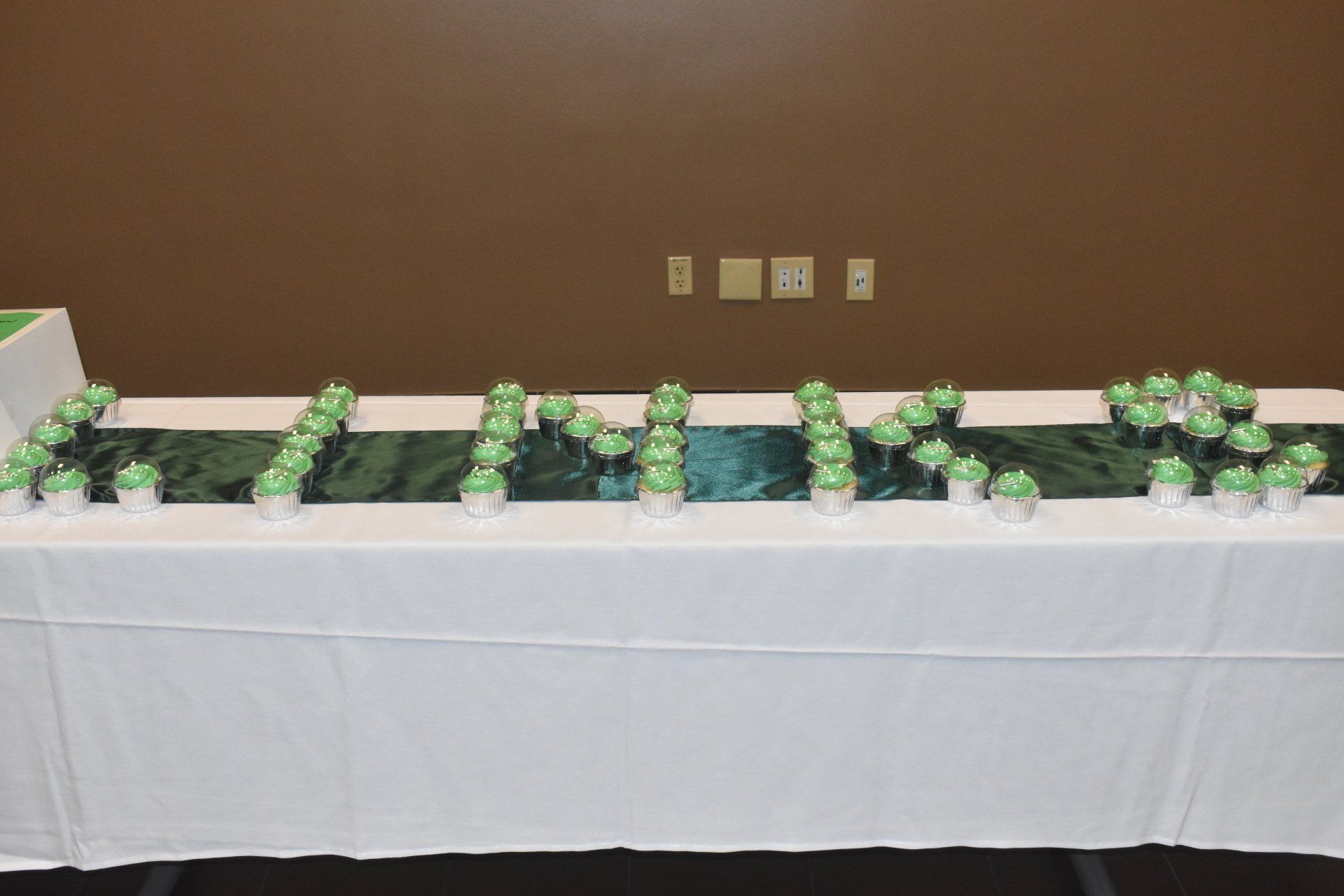 Cupcakes arranged on a white-covered table spell out the word 