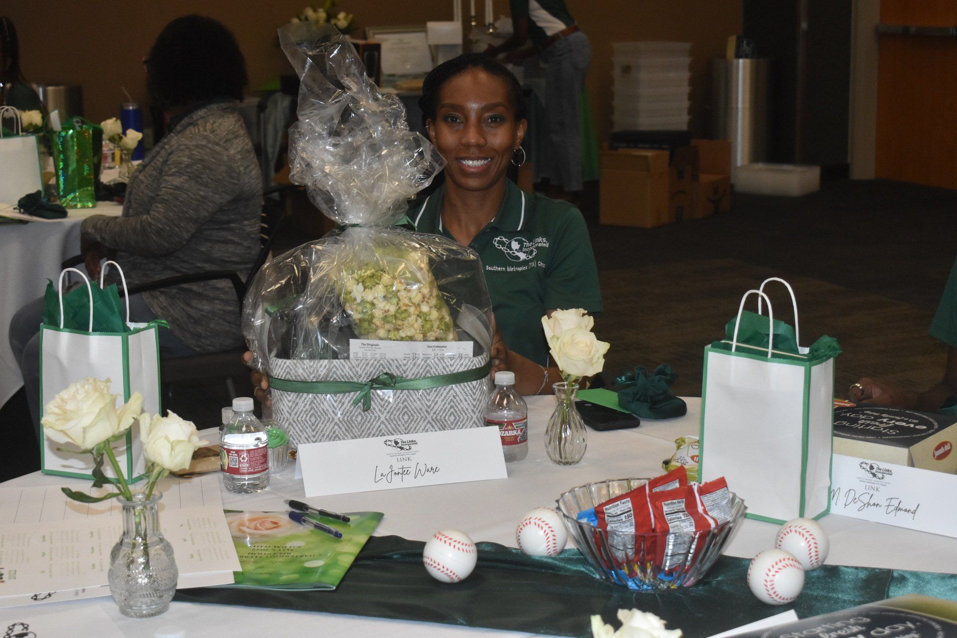 Woman at a decorated table smiles. A gift basket, baseballs, and flowers are on the table.