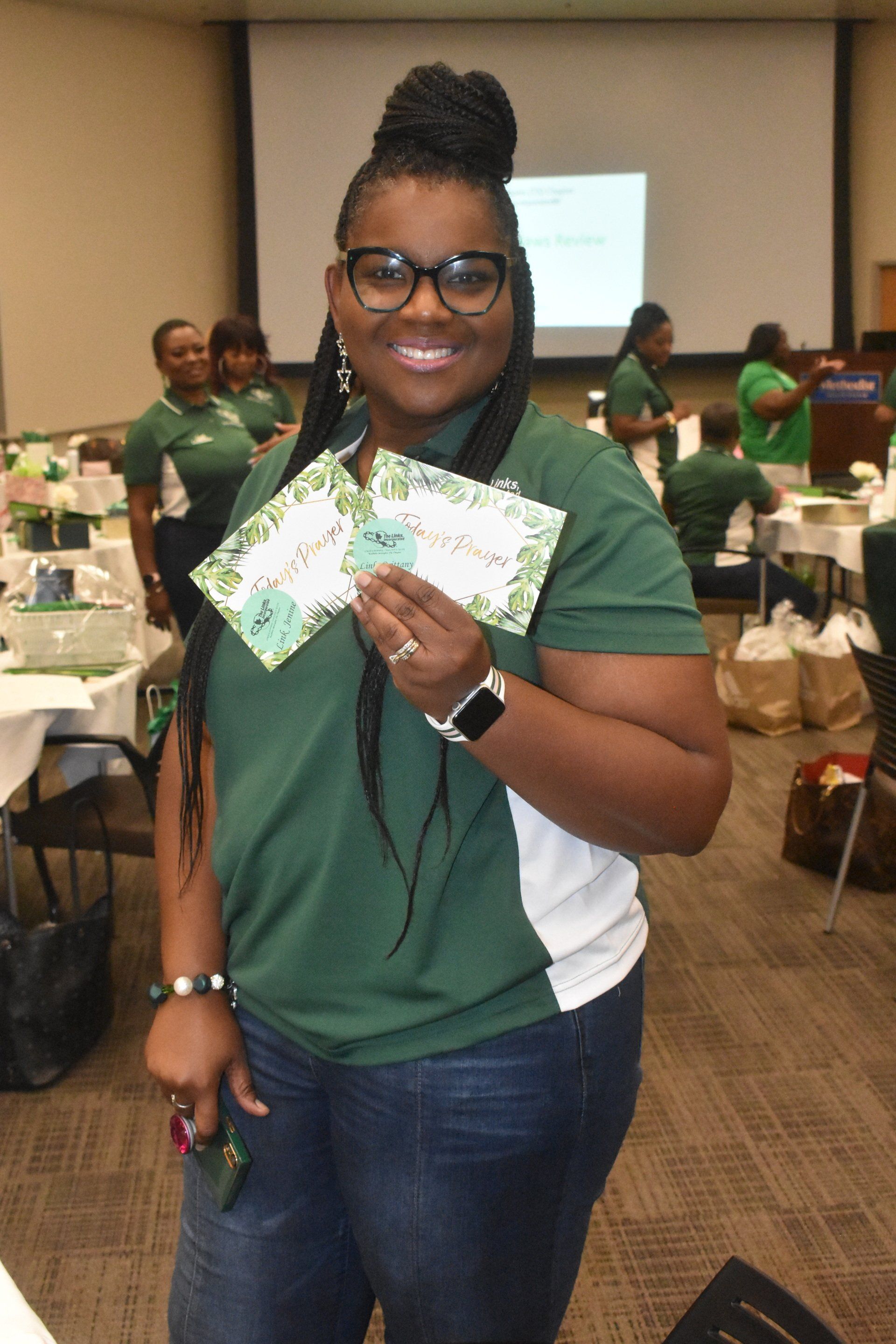 Woman in green shirt holding cards, smiling in a conference room.