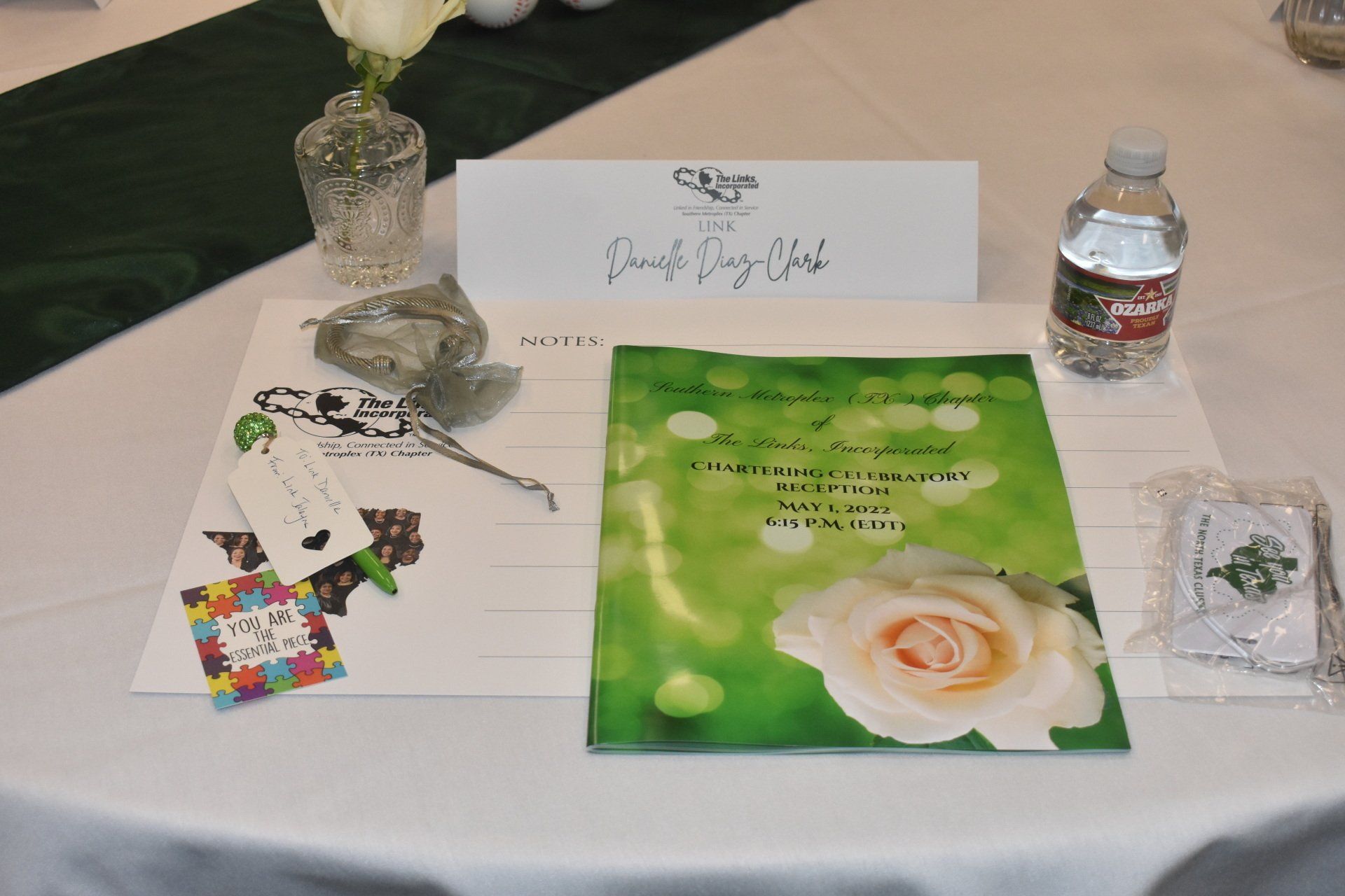A table set with a floral arrangement, guest name card, program, water bottle, and party favors.