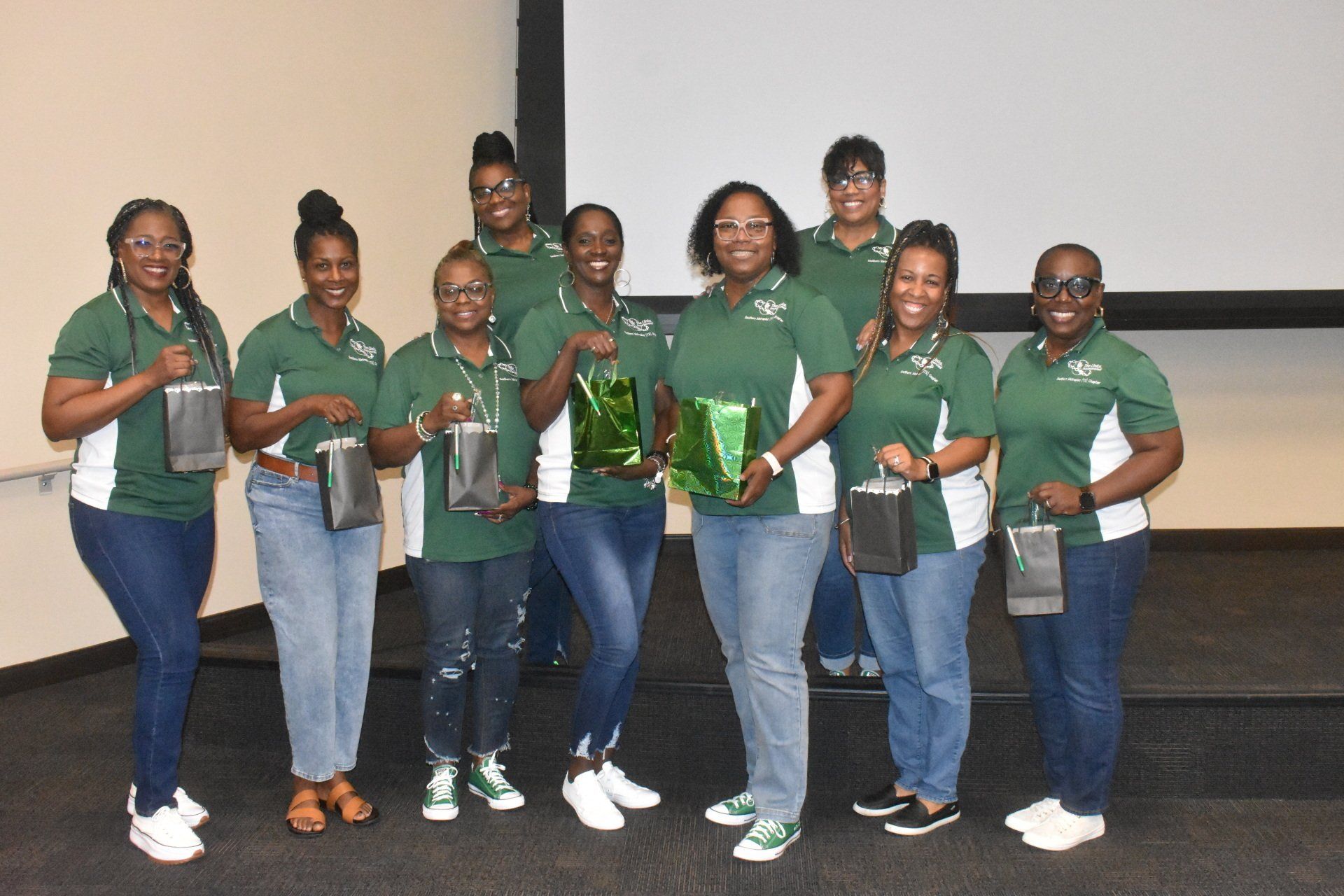 Group of people in green shirts holding gifts, posing together.