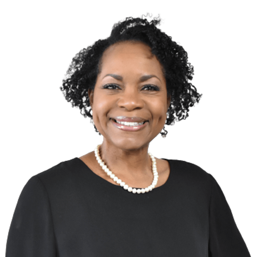 Woman with curly dark hair, smiling, wearing a black top and pearl necklace.