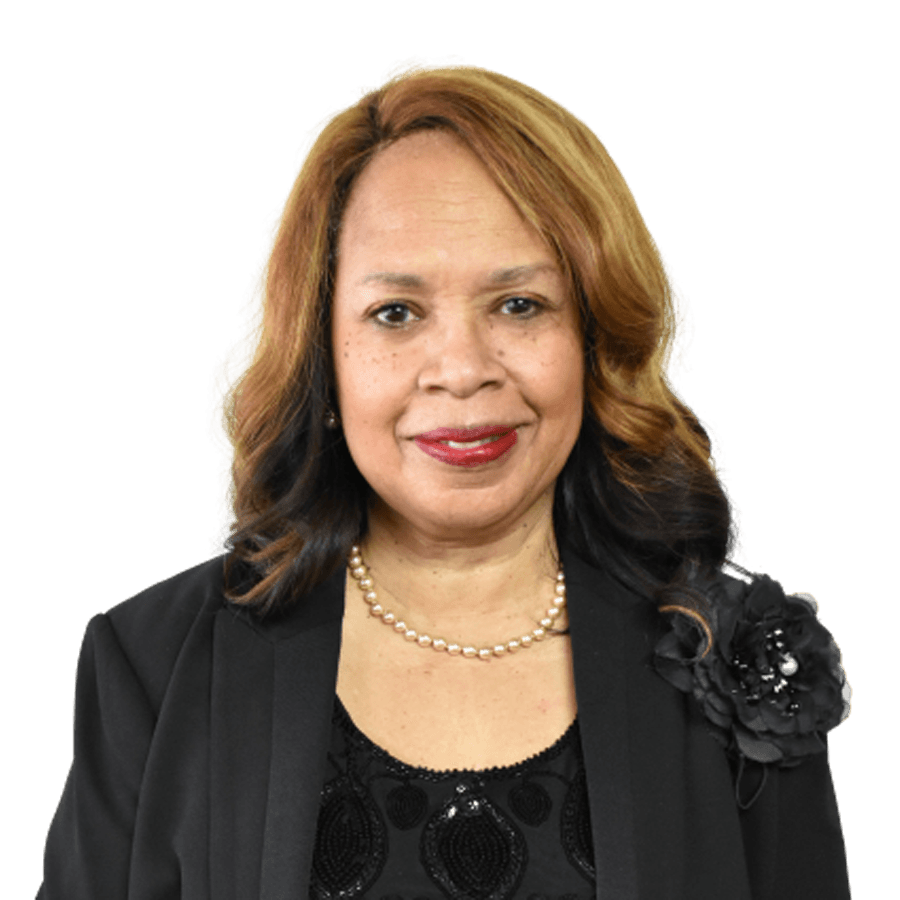Woman in black suit and pearl necklace smiles, with auburn and black hair against a white background.