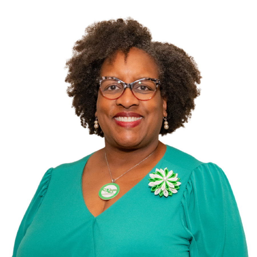 Woman with curly hair, glasses, and green top smiles, wearing a green and white pin and necklace.