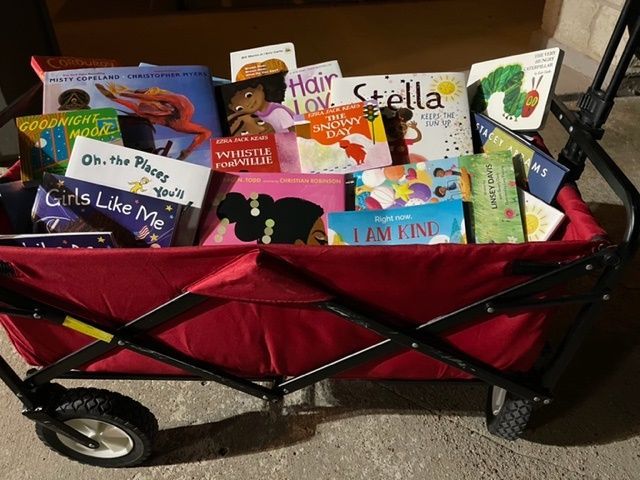 Red wagon filled with children's books, titles visible. Wheels and metal frame are black.
