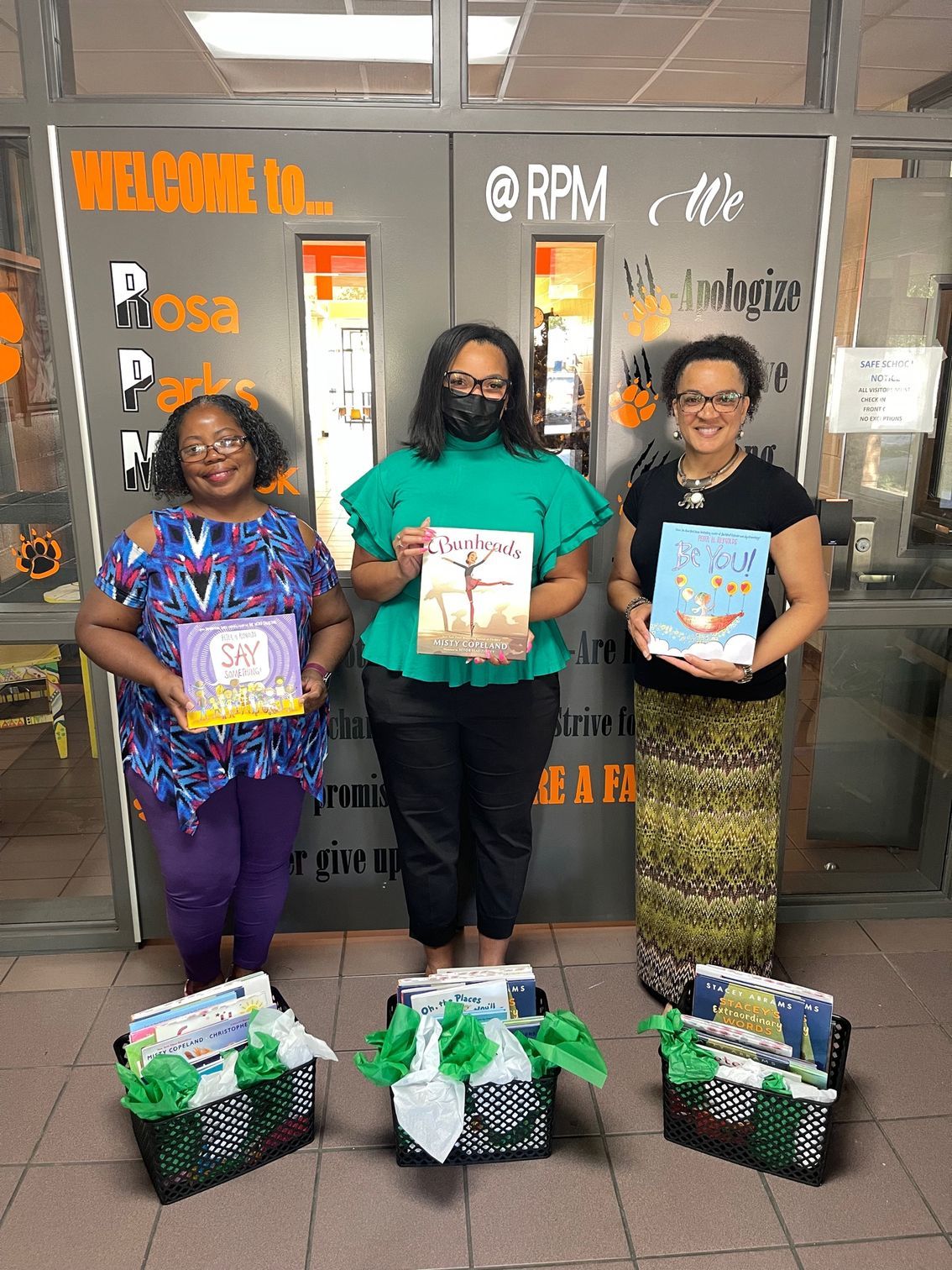 Three women holding books, posing by a door with baskets of books. Green and orange accents.