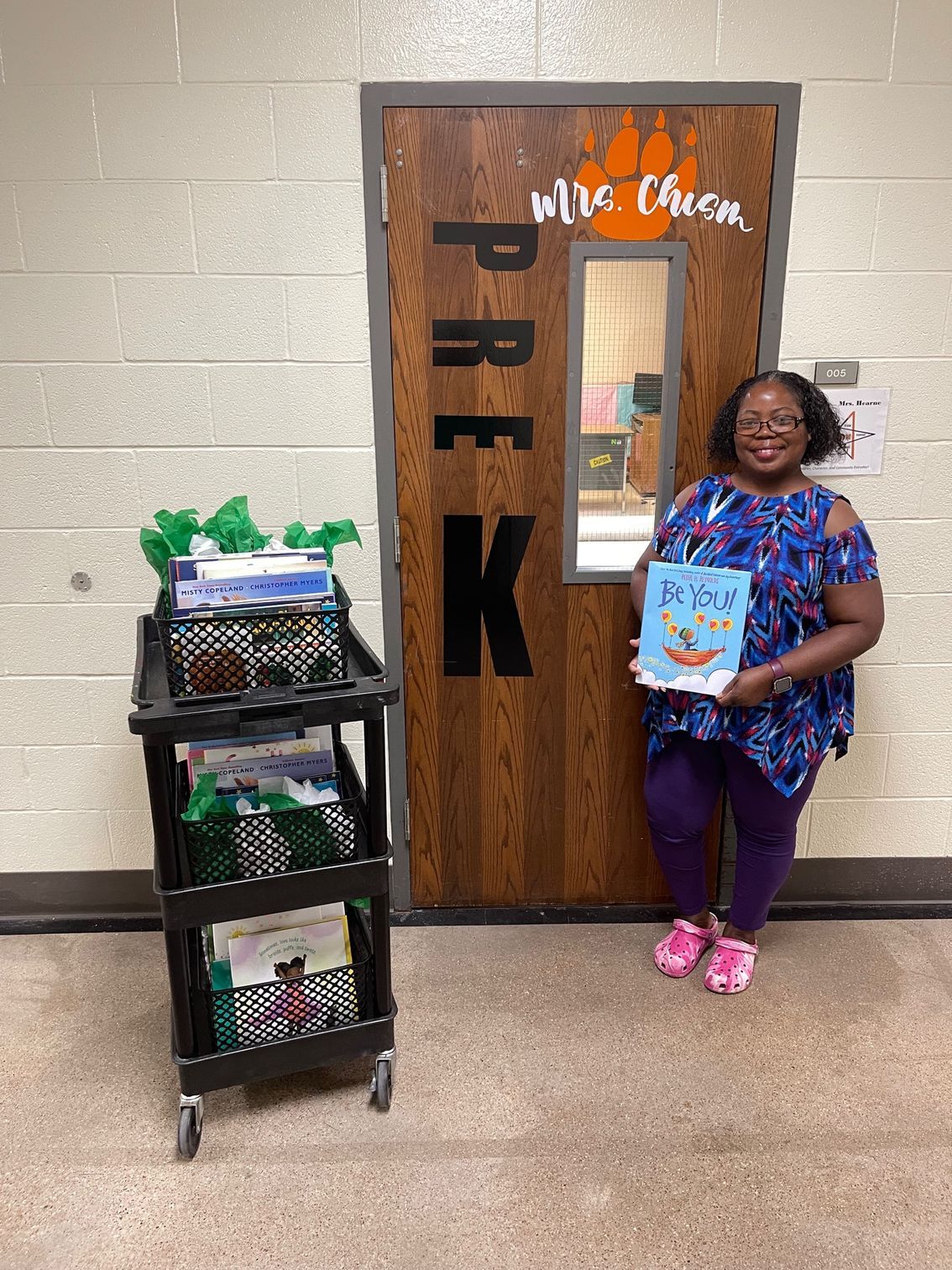Woman holding a book in front of a classroom door labeled 
