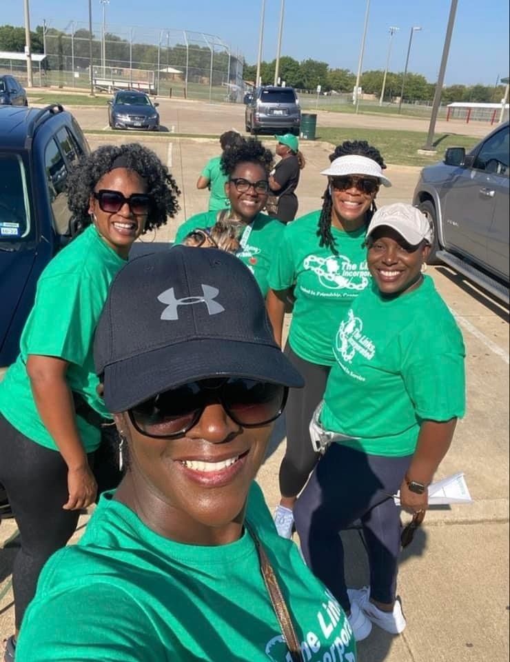 Five people in green shirts smile, posing for a selfie outside.
