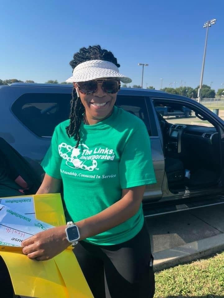 Woman in green shirt and visor holds papers by car, smiling outdoors.