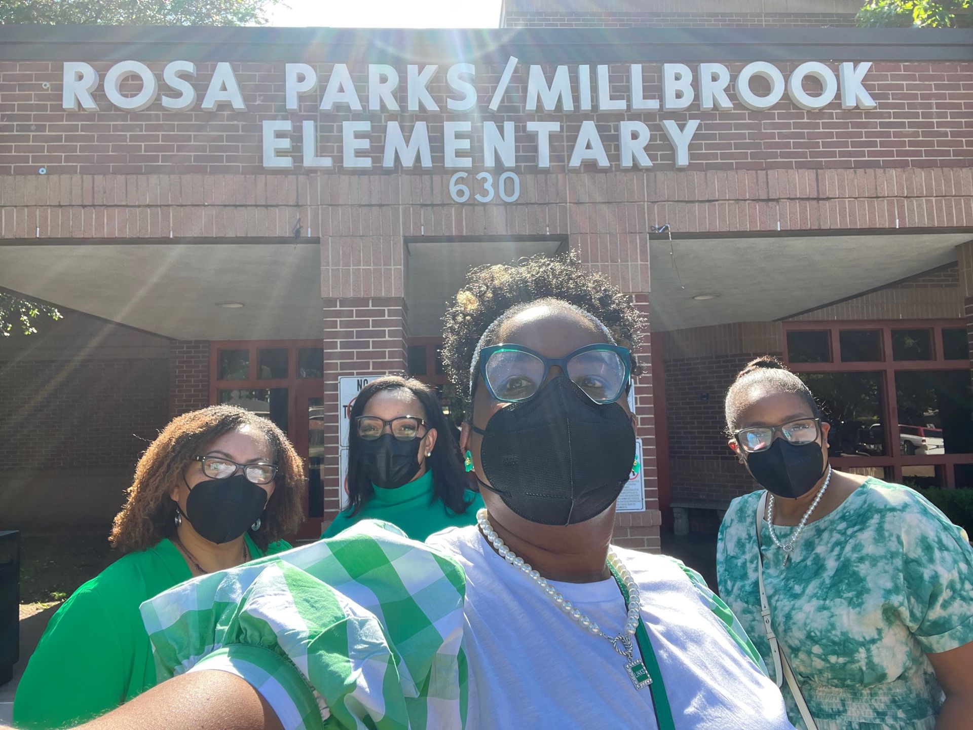 Four people in masks in front of Rosa Parks/Millbrook Elementary School building.