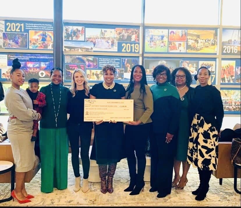 Group of women holding a large check indoors, standing in front of a timeline.