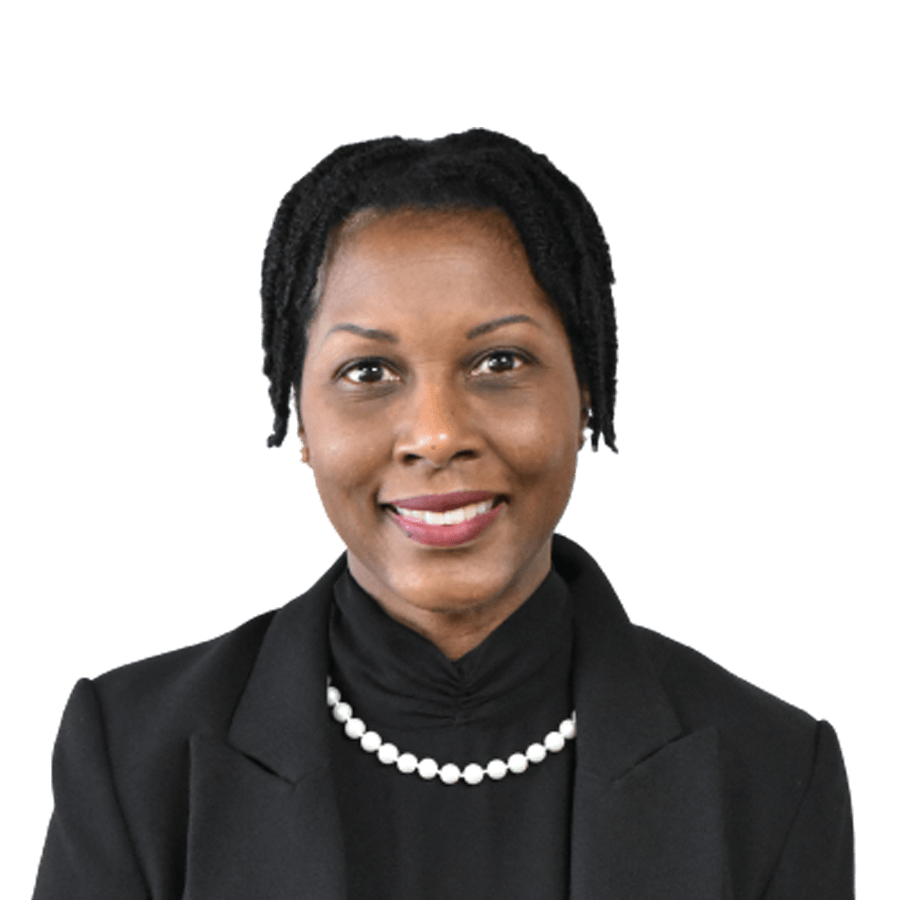 Woman in a black blazer and pearls smiles, against a white backdrop.