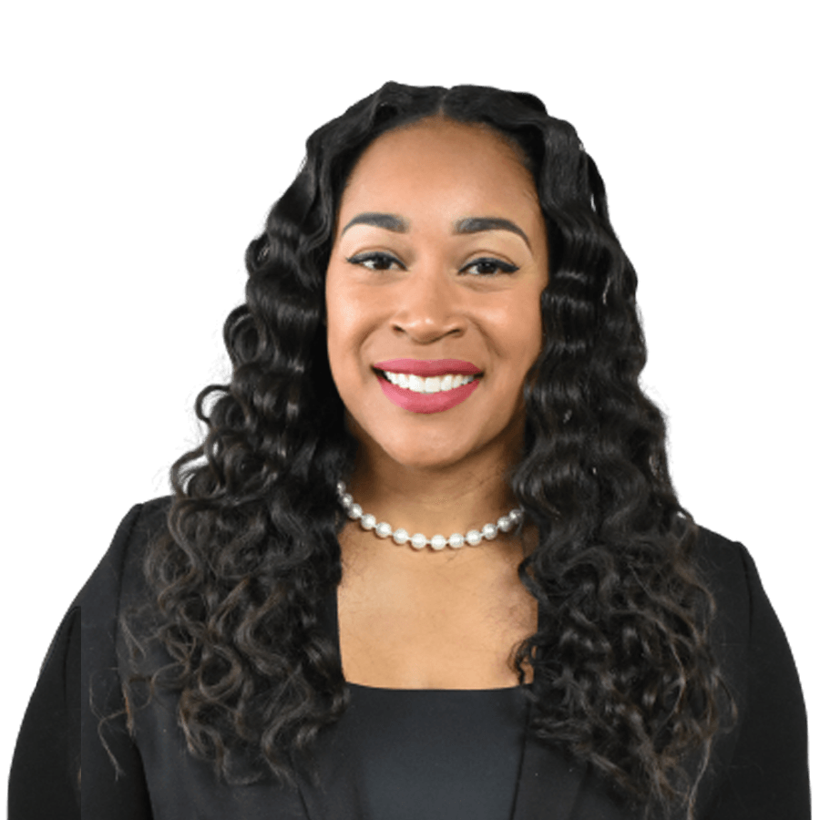 Woman with long, wavy dark hair smiles wearing a black blazer and pearl necklace.