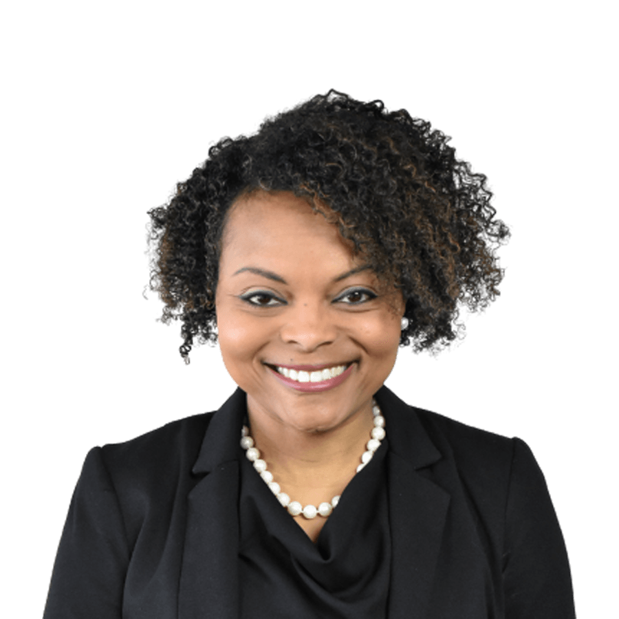 Woman with curly hair, wearing a black blazer and pearl necklace, smiling.