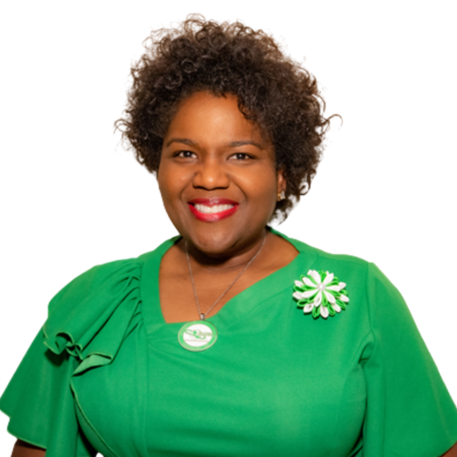 Woman wearing a green dress with a flower brooch and necklace smiles, head and shoulders shot.