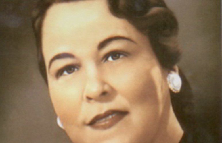 Woman with dark hair, wearing pearl earrings, looking towards the camera.