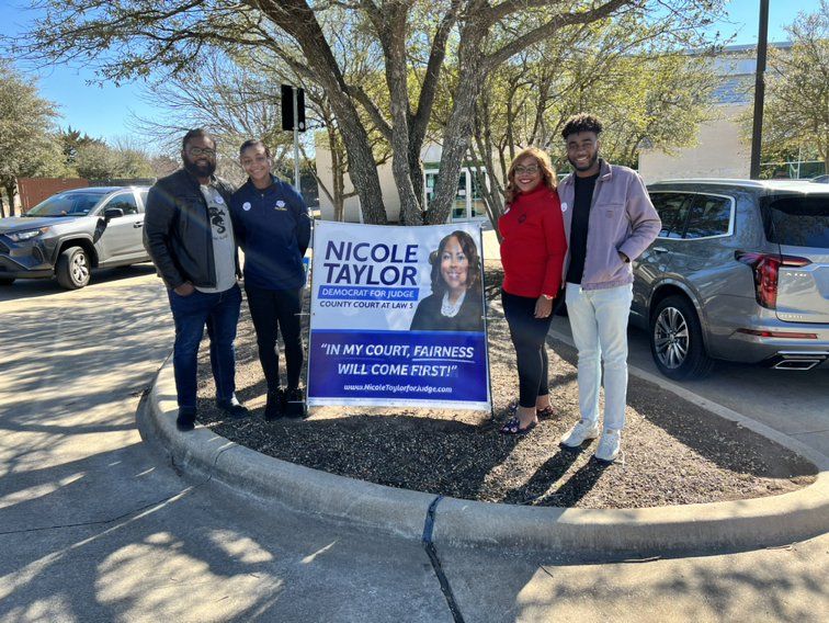 Five people stand by a sign that reads “Nicole Taylor for Justice.” The sign has a photo of Taylor.